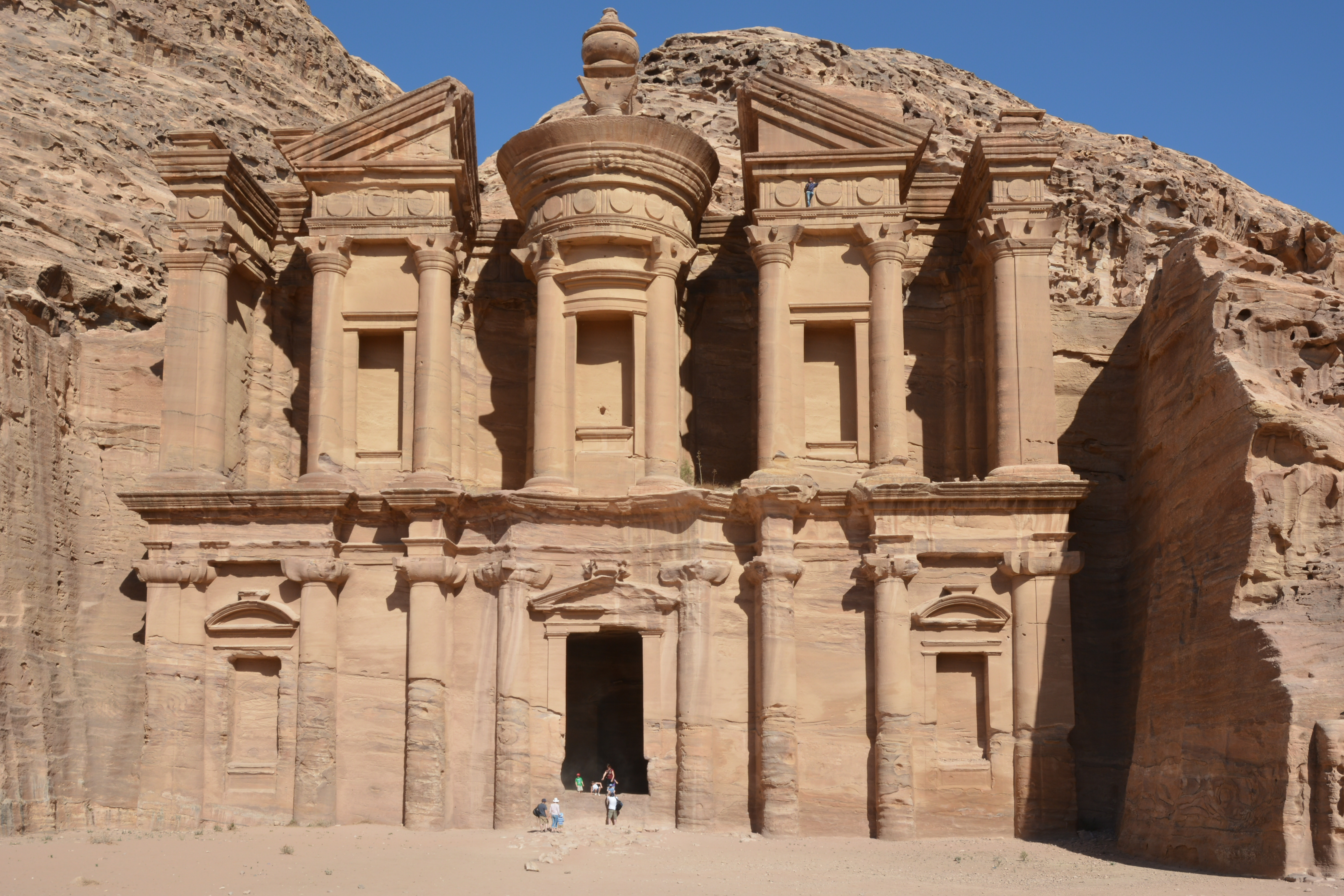Al Deir, "The Monastery", a monument closely resembling Al Khazneh though less ornate. It can be accessed climbing a long flight of stairs carved in the mountain above Petra. A man can be seen at the top of the facade, slightly on the right of the picture.