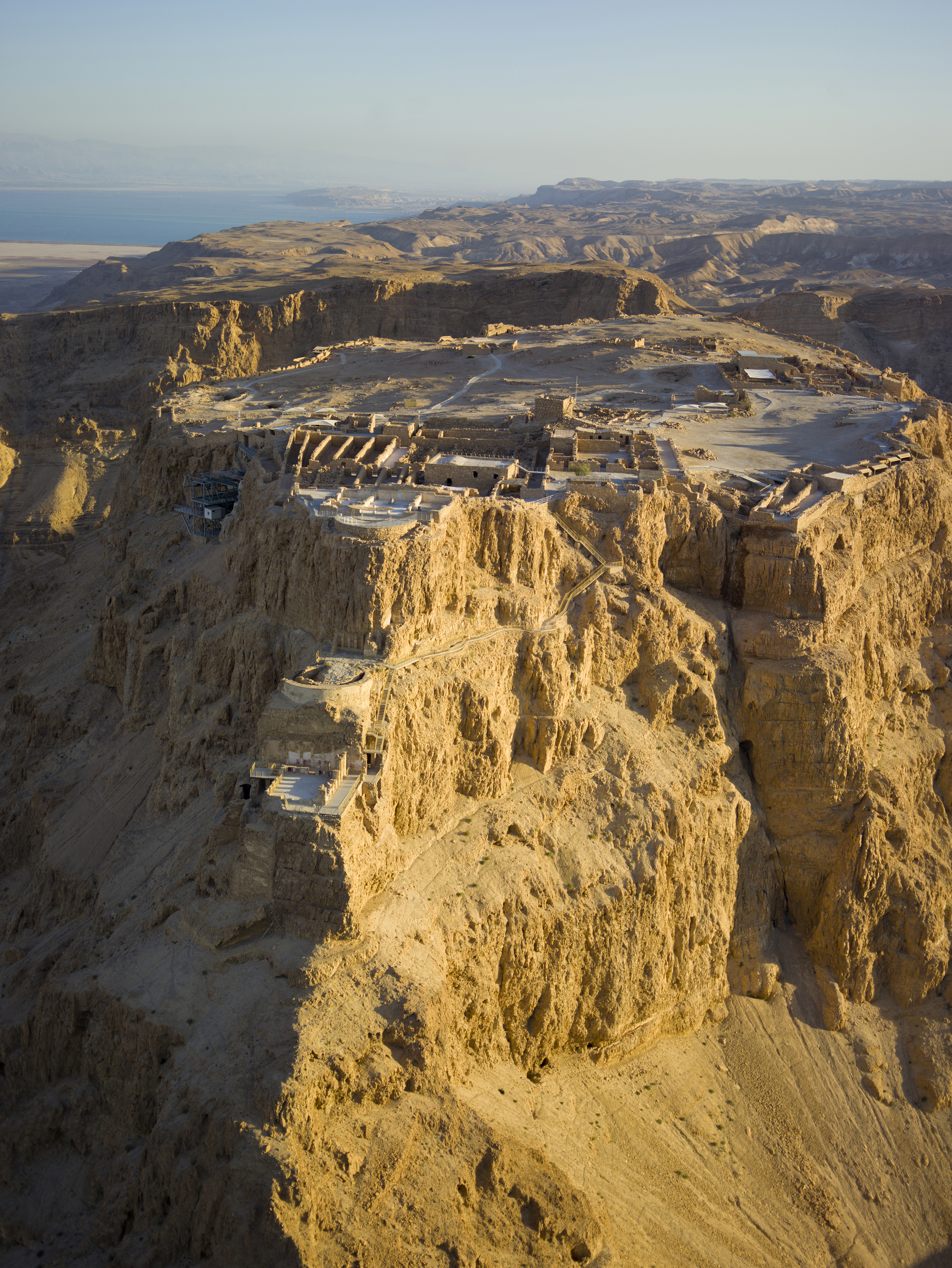 Aerial view of Masada (Hebrew מצדה), in the Judaean Desert (Hebrew: מִדְבַּר יְהוּדָה‎, Arabic: صحراء يهودا), with the Dead Sea in the distance.