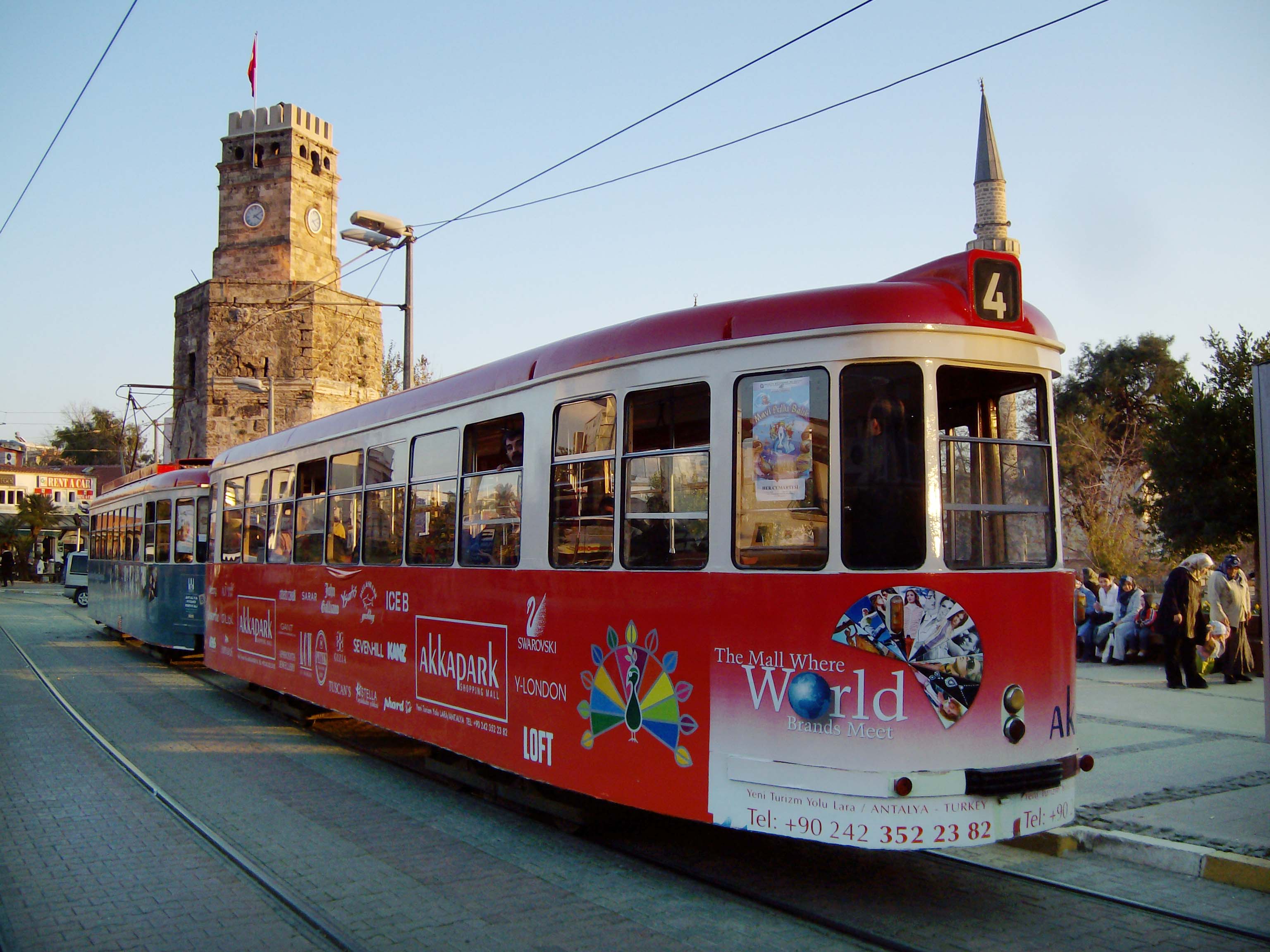 Antalya .tr – Straßenbahn vor der Kulisse des Uhrenturms und dem Minarett der Mehmet-Pasa-Moschee.