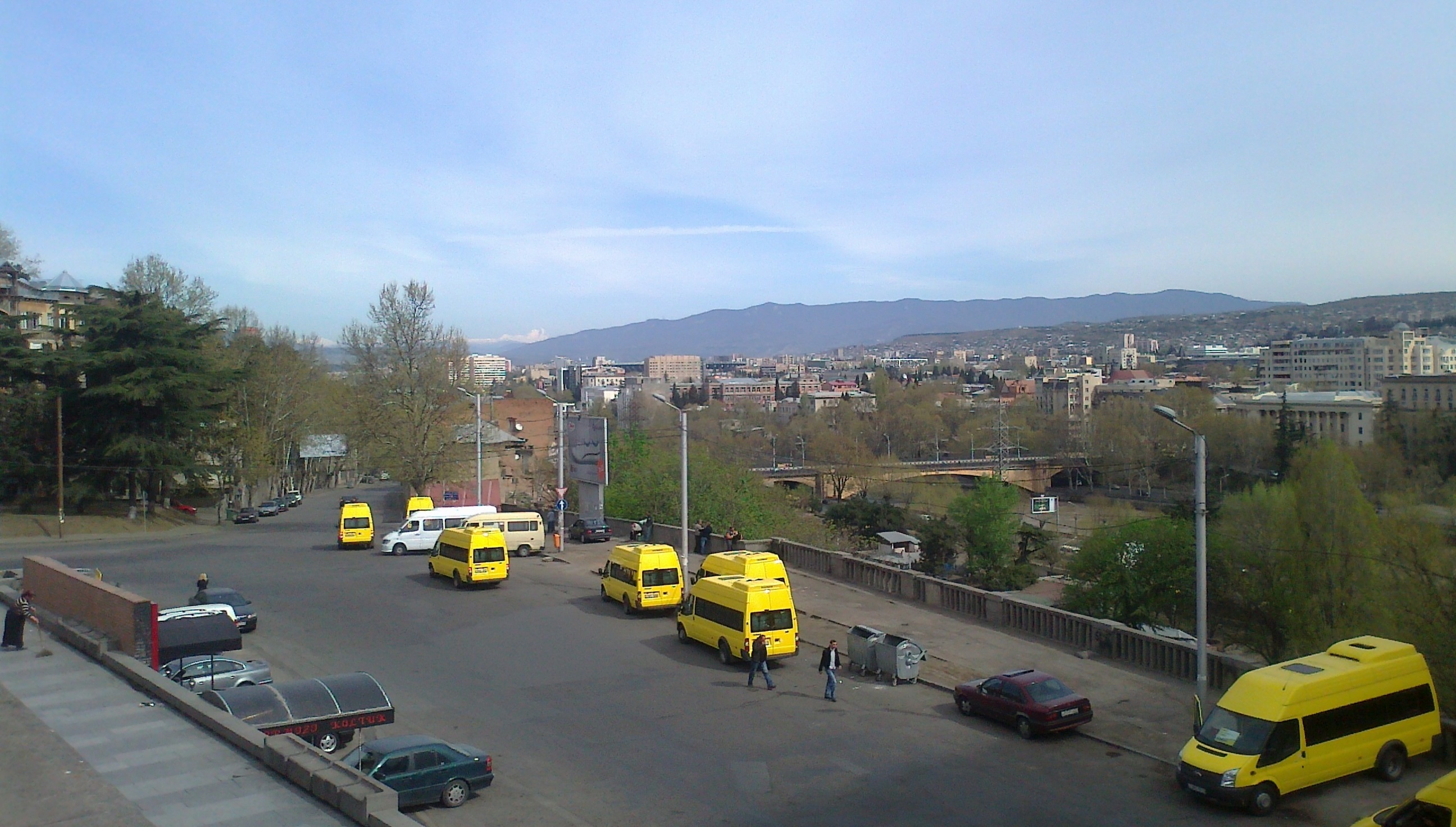 The so-called "yellow" minibuses close to M. Javakhishvili Street. A view from Square of the Roses, Tbilisi. The Caucasus mountains are seen in the distant left background.