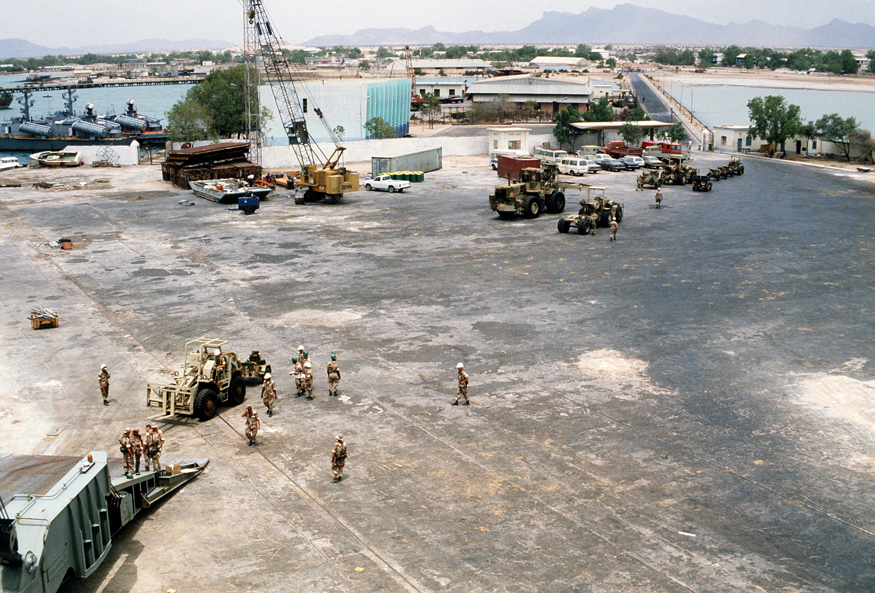 U.S. Marine Corps equipment is offloaded from the container ship SS LYRA during Exercise Eastern Wind '83, the amphibious landing phase of Exercise Bright Star '83. Two Somali navy project 205-ER type 21 missle boats (NATO code - Osa II Class fast attack craft) are visible in the upper left. The names of boats were №125 and unknown. Location: Berbera.