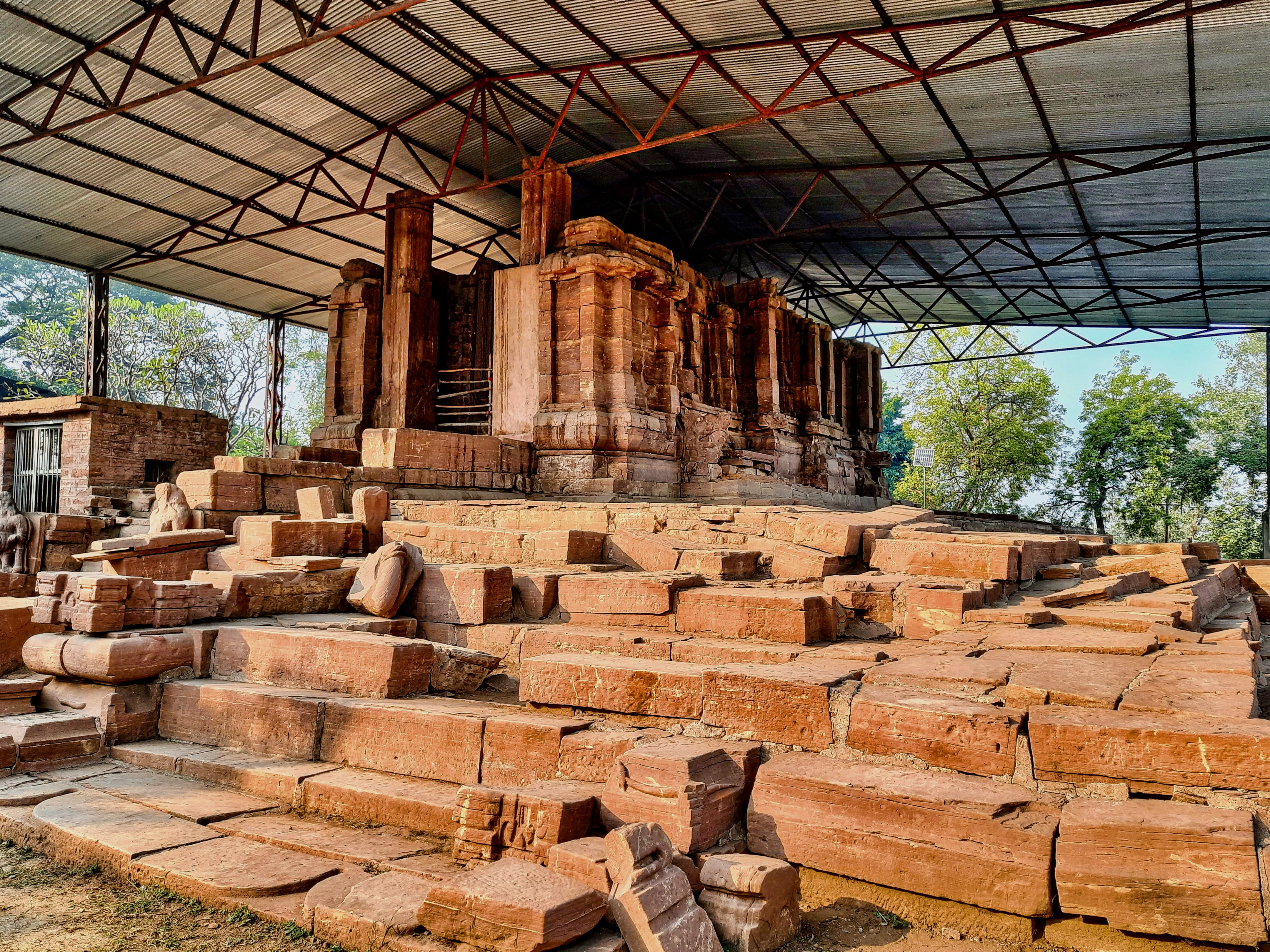 The Tala site in Chhattisgarh is a collection of major Hindu temples and ruins from the early 6th century (c. 525 CE), making it one of the oldest known Hindu monuments in Chhattisgarh that have survived into the modern age. Before 1950, colonial era British and Indian archaeologists knew of scattered ruins and a large mound at Tala. The site was finally excavated and studied in the late 1970s through 1980s, thus unearthing the scale and significance of the Tala site.
The Devrani Jethani temples site is located on the eastern banks of the Maniyari river, near a Hindu pilgrimage site and collection of modern era temples. The historic site consist of two temples made from sandstone. The larger Jethani temple is mostly in ruins. The smaller Devrani temple is more intact but also ruined. They are next to each other, and their modern era names mean "elder daughter-in-law" and "younger daughter-in-law" in many Indian languages, signifying that they are housed together, related and yet one is bit older and bigger. Both temples are under a shed (added in the 2010s) to prevent erosion from rain. A small museum at the site holds some of the better preserved 6th-century sculpture of Shaivism, Vaishnavism, Shaktism traditions, as well as Vedic deities.
The Jethani temple is quite large, spreads over 10000 square feet, with a platform and four stepped entrances. Huge damaged and fallen pillars, life size to larger than life size statues, naturally eroded structures, and some deliberately damaged Hindu artwork is visible. Of these, the bharavahakas (sculpted weight bearers below structural elements) are impressive as they facial expressions humorously show the dwarfs feeling the pressure of massive structure above them.
The better preserved Devrani temple is the oldest standing Hindu temple that can reliably dated to be from the ancient Kosala region mentioned in Indian epics. The dating is based on short inscriptions found here in a script style that existed prior to the 7th century. Further, the artwork here are of the quality found in some Gupta era sites in Madhya Pradesh and Vakataka era sites in eastern Maharashtra – both known to have flourished between the 3rd and 6th centuries. Thus, the Tala site has contributed a better understanding of art, Hindu iconography and creative innovation by about 550 CE in central and Deccan region of ancient India.
Tala enigmatic statue – a masterpiece of innovative creativity was unearthed in 1988. It is a stone statue about 5 tons in weight and larger than life (8 feet high), from a single rock, very likely produced at site with the temple. The exceptional aspect of the statue is that most of the man's visible body parts are other living beings. Snakes form his hair and a turban, a lizard forms his nose, lizard's hind legs form the brows, a frog his eyes, two fishes form his moustache, a crab shapes his chin and lip, two peacocks help form his ears, busts of two crocodiles shape his shoulder, a turtle his penis (in urdhvareta form, or ithyphallic), two lion cubs form his two knees, and so on. From fingers to toes, from a carefully interrelated fusion of living beings emerges the shape of a well built man. Further, many faces are carved on his chest and stomach. Since its discovery in 1988, scholars have offered many interpretations as to what this statue represents and signifies, particularly in light of the fact that it too is dated to early 6th century. Some suggest it to be a form of Shaiva and Vaishnava Hindu traditions, particularly Sadashiva, Matsya, Kurma, Narasimha and others avatars. An alternate theory is that the creature forms selected may be the vahanas of Hindu gods and goddesses, the artist thus implies and fuses the many gods and goddesses carried into one within the human form. There is no consensus yet. This Tala enigmatic statue stands in front of the Devrani temple and to the left of the steps that lead to its platform. This is where it was found.
The temple ruins, various artwork including the enigmatic statue attract reverential offerings and treated as a place for worship from the regional Hindus. It is also a tourist attraction, well connected with modern highways. The site is a declared national monument, under the protection and management of the ASI.
