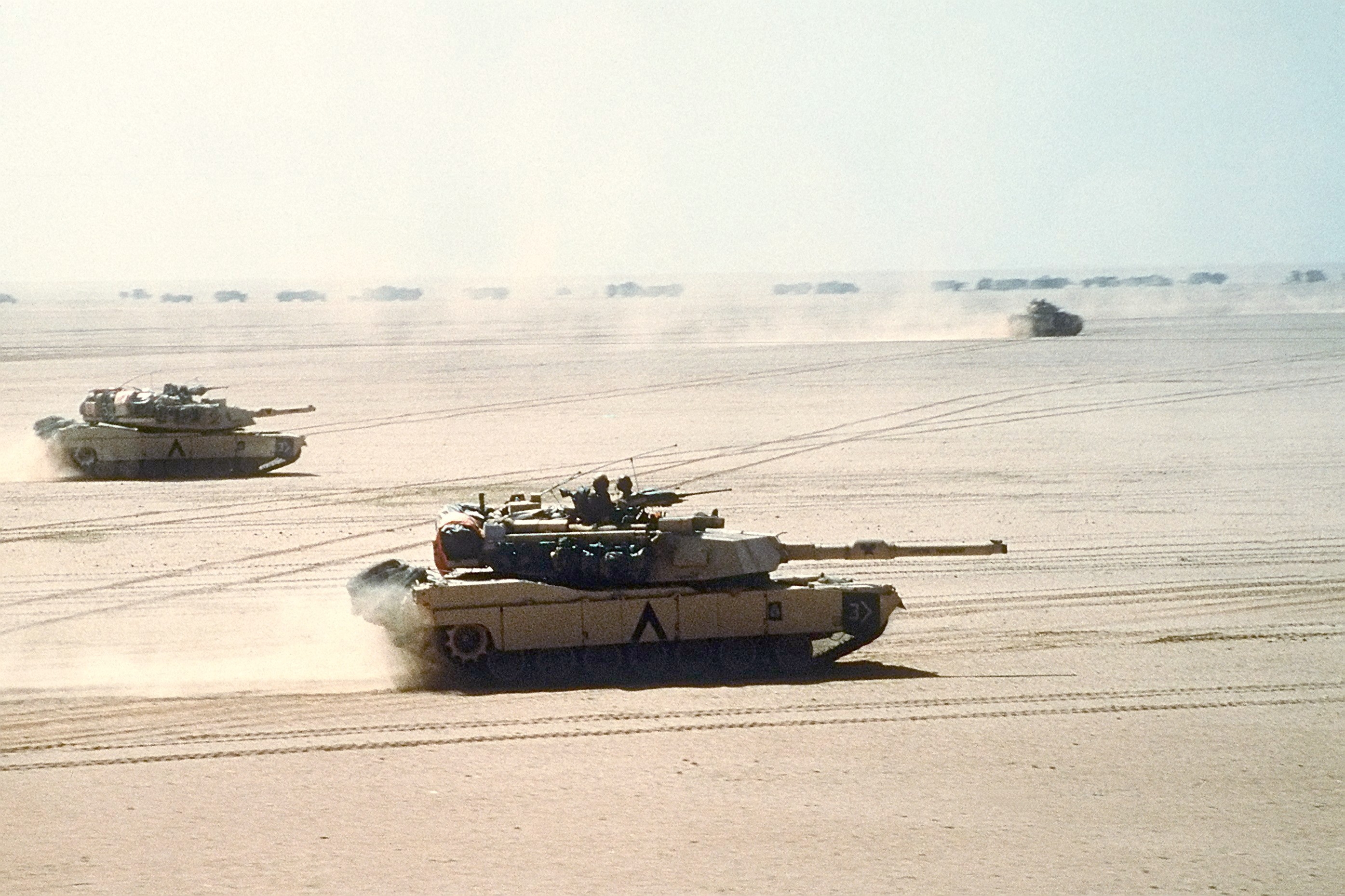 M1A1 Abrams main battle tanks of the 3rd Armored Division move out on a mission during Operation Desert Storm. An M2/M3 Bradley can be seen in background.