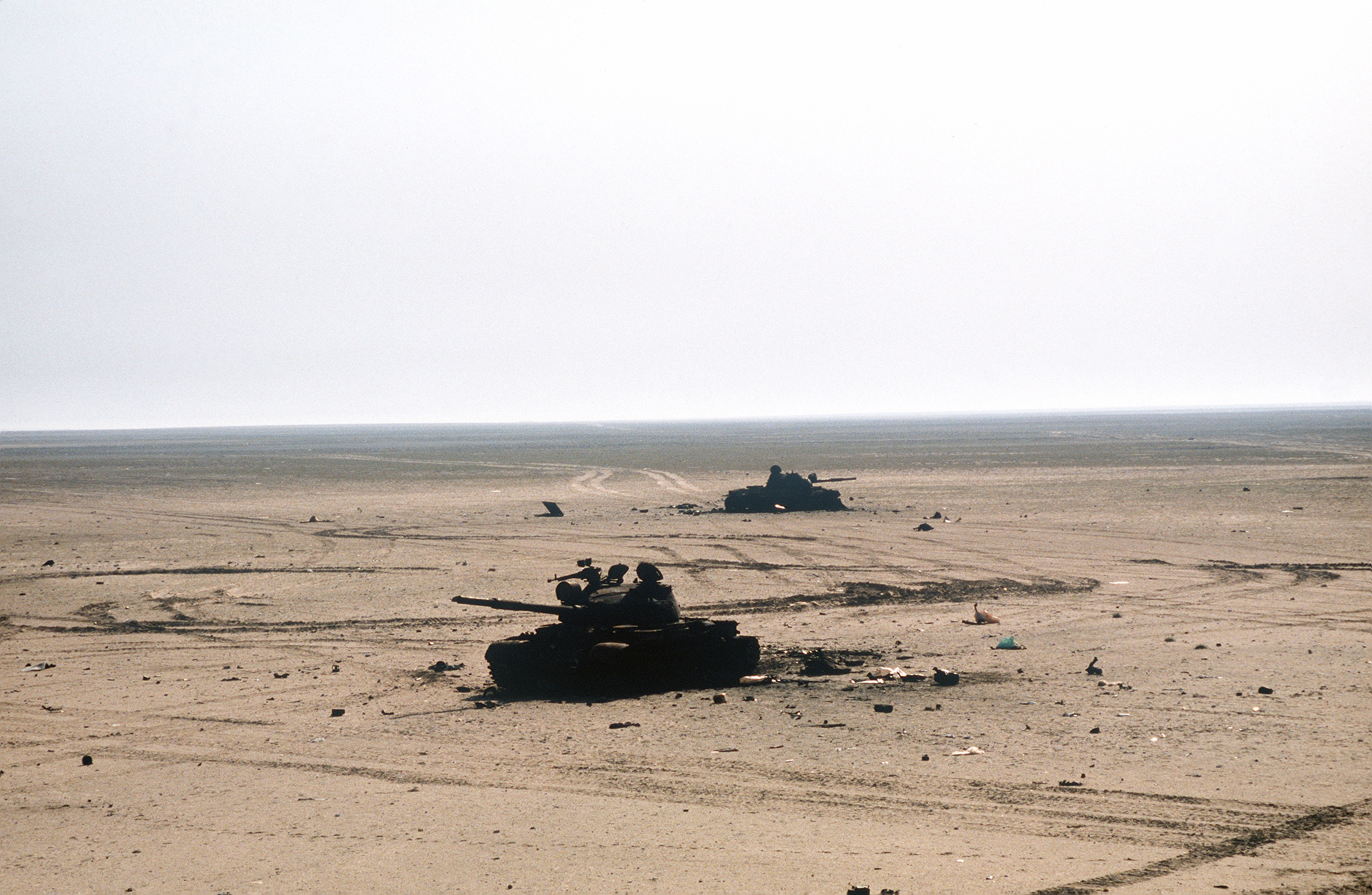 Two destroyed Iraqi T-62 main battle tanks lie in the sand beside a road during the ground phase of Operation Desert Storm.