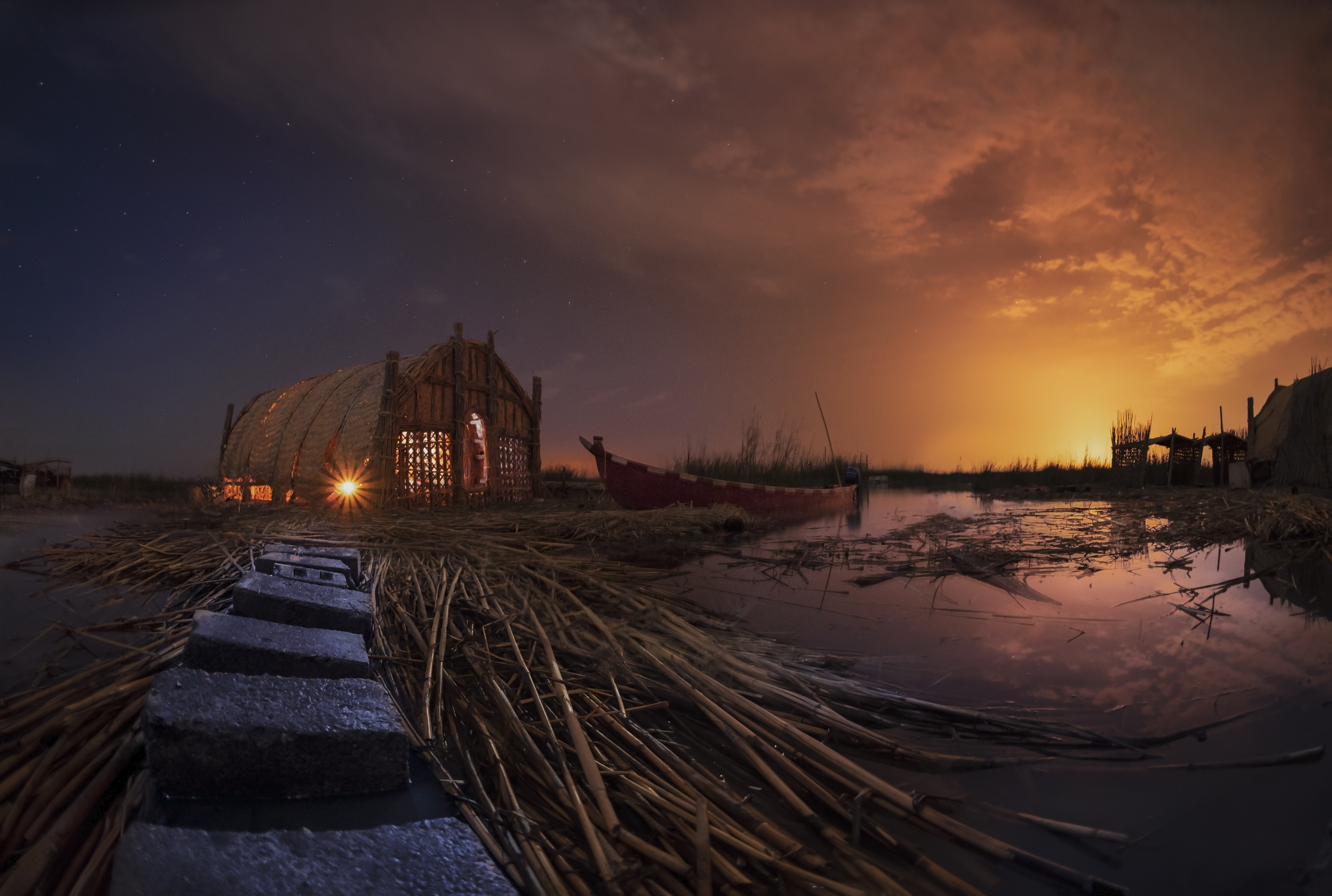 Mesopotamian Marshes of Iraq at night: reed house Mudhif, narrow canoe Mashoof &amp; water.