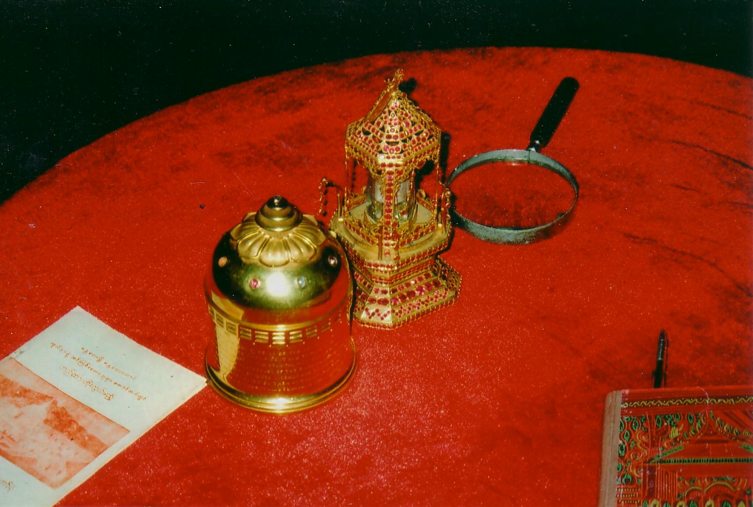This picture is of the ruby and gold relic casket holding a crystal reliquary with three fragments of bone, believed to be relics of Gautama Buddha, buried by the Kushan Emperor Kanishka in the 2nd century A.D. at his stupa in Peshawar (now in Pakistan) from where they were sent by the British for safekeeping to Mandalay, Burma in 1910. To the left of the ruby and gold casket is a miniature golden stupa in which the relics were transported to Mandalay