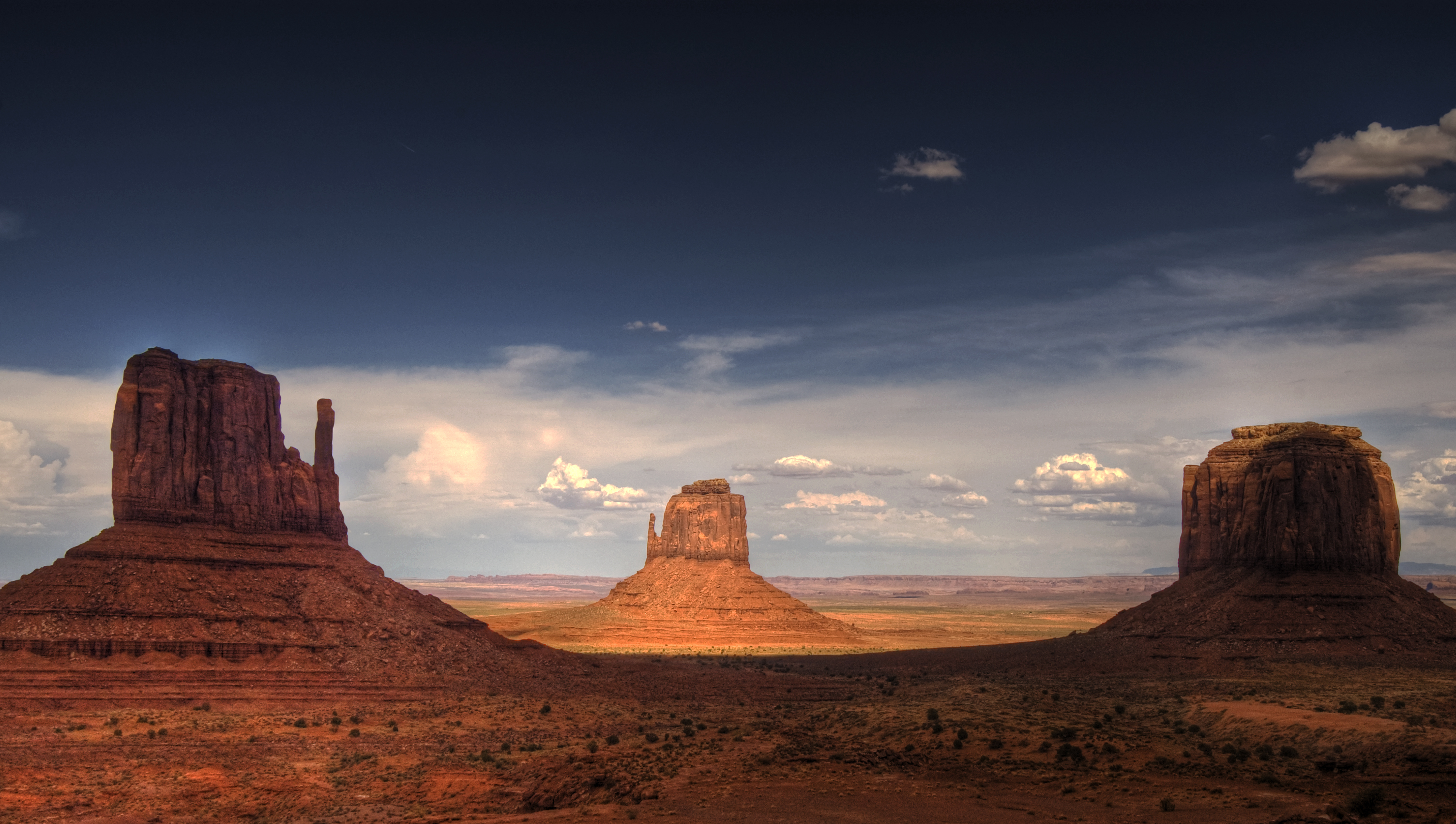 Monument Valley, the buttes are clearly stratified, with three principal layers. The lowest layer is Organ Rock Formation-(skirts, slope-former), the middle De Chelly Sandstone-(vertical cliffs) and the top layer is Moenkopi Formation (shales?, horizontal bedding) capped by Shinarump siltstone-(Shinarump Conglomerate-(locally)). The 3 buttes lie in Arizona, adjacent the Utah border. The en:West and East Mitten Buttes (left &amp; center) are about 1.5 miles (2 km) apart. Merrick Butte is at photo-right.