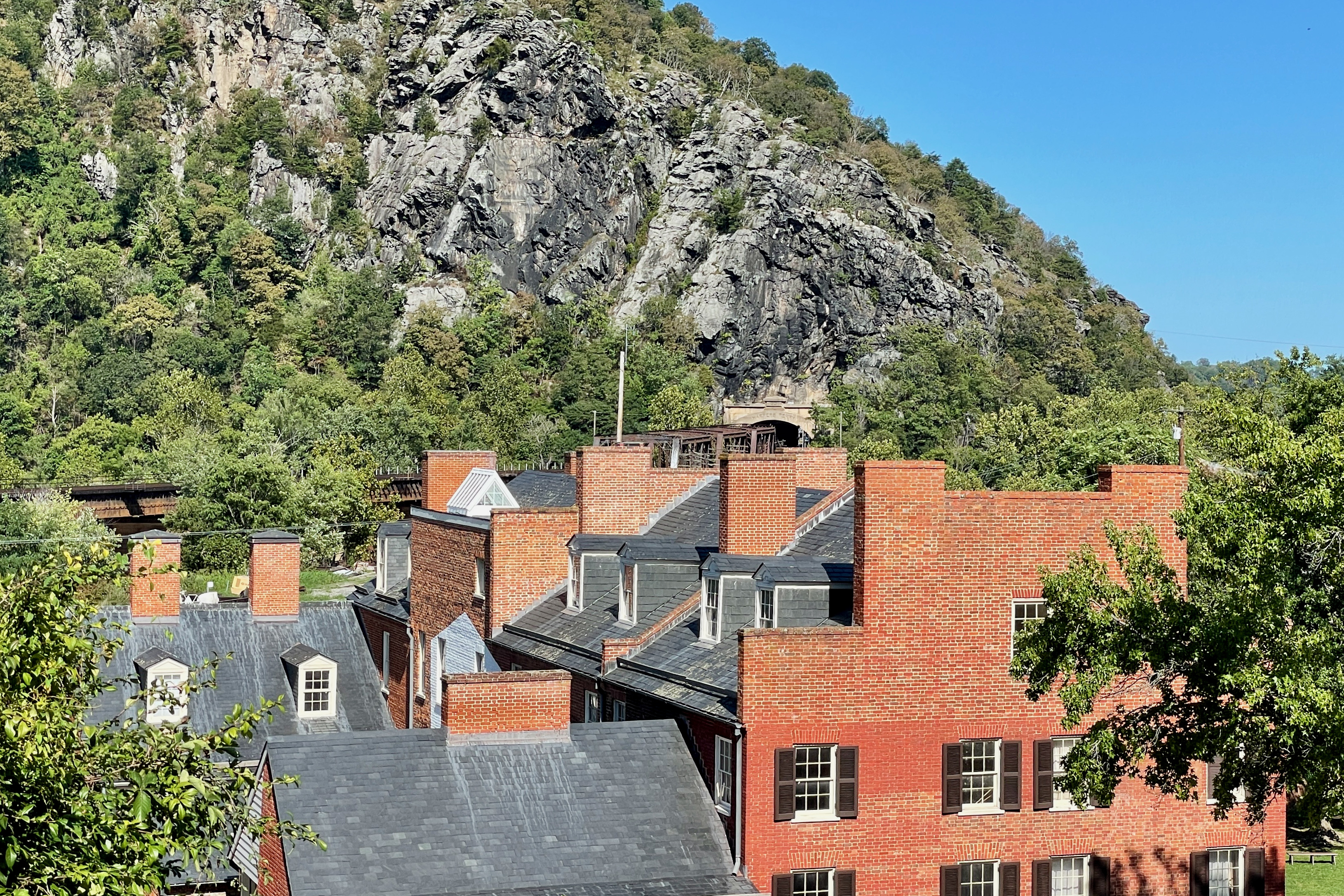 View of brick buildings in the Lower Town section of Harpers Ferry, West Virginia with Maryland Heights and the B &amp; O Railroad Potomac River Crossing in the background. The Mennen's Borated Talcum Toilet Powder advertisement can be seen on the cliff face. Part of the Harpers Ferry National Historical Park.
