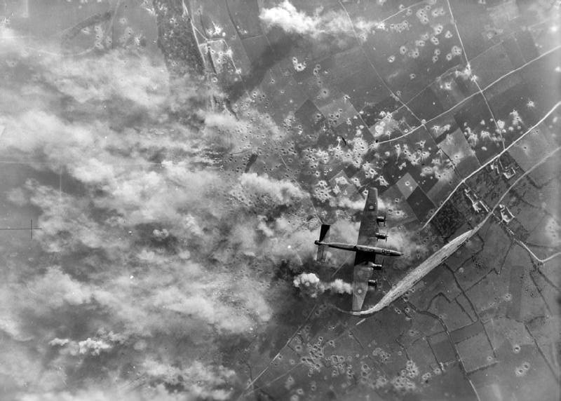 Vertical aerial photograph taken during the daylight attack on the German secret weapon (V3) site at Mimoyecques, near Marquise, France, showing a Handley Page Halifax flying over the target as exploding bombs send smoke and clouds of dust into the air.