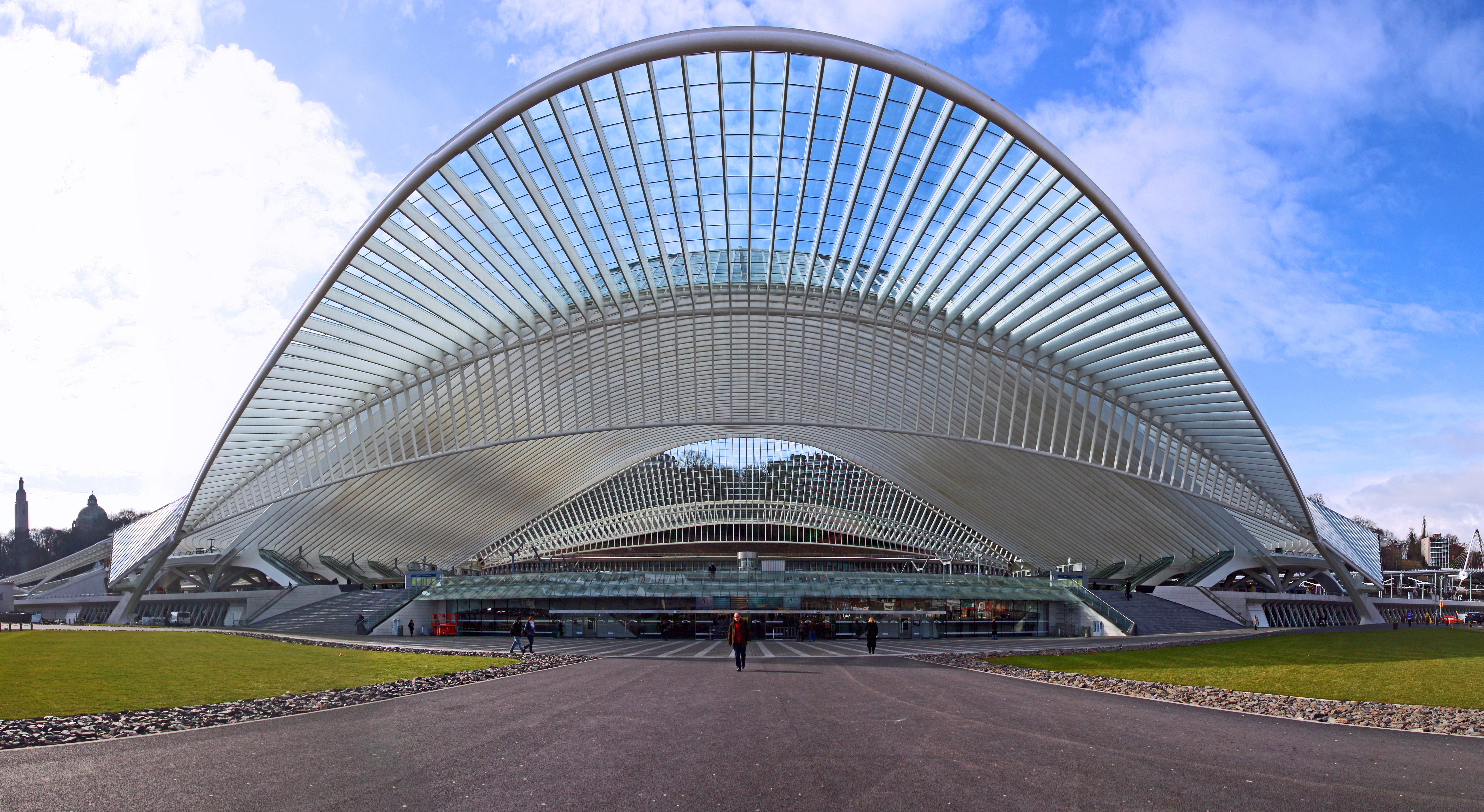 Station / Gare Liège-Guillemins is the main station of the city of Liège, in eastern Belgium. It is one of the most important hubs in the country and is on the high-speed train network. The station is used by 36,000 people every day.
In 1838, only three years after the first continental railway, a line linking Brussels and Ans, in the northern suburbs of Liège, was opened. The first train station of Liège-Guillemins was inaugurated in May 1842, linking the valley to the upper Ans station. In 1843, the first international railway connection was born, linking Liège to Aachen and Cologne.
The station was modernized and improved in 1882 and in 1905 for the World Fair in Liège. This station was replaced in 1958 by a modern (for that time) one that was used until June 2009, a few months before the opening of the new Calatrava designed station.
The new station by the architect Santiago Calatrava has now been openend. It has 9 tracks and 5 platforms (three of 450m and two of 350m). All the tracks around the station have been modernized to allow high speed arrival and departure.

The new station is made of steel, glass and white concrete. It includes a monumental dome, 200 meters long and 35 metres high. The building costs were € 312 million. The station was officially opened on September 18 2009 with a show by Franco Dragone
