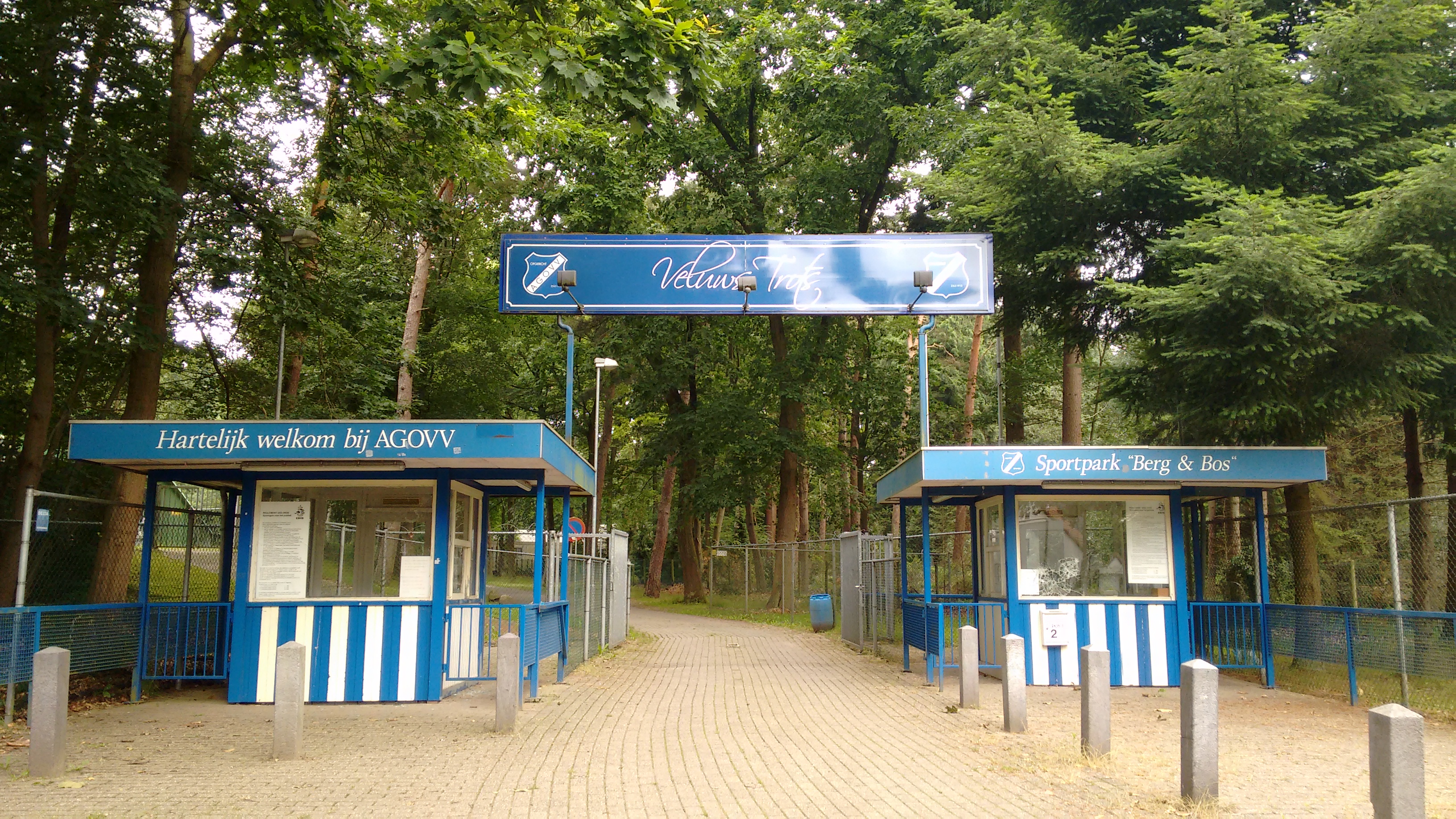 De entree van Sportpark Berg &amp; Bos van voetbalclub AGOVV (Apeldoorn). Teksten: 'Hartelijk welkom bij AGOVV', 'Veluws Trots', 'Sportpark "Berg &amp; Bos"'.