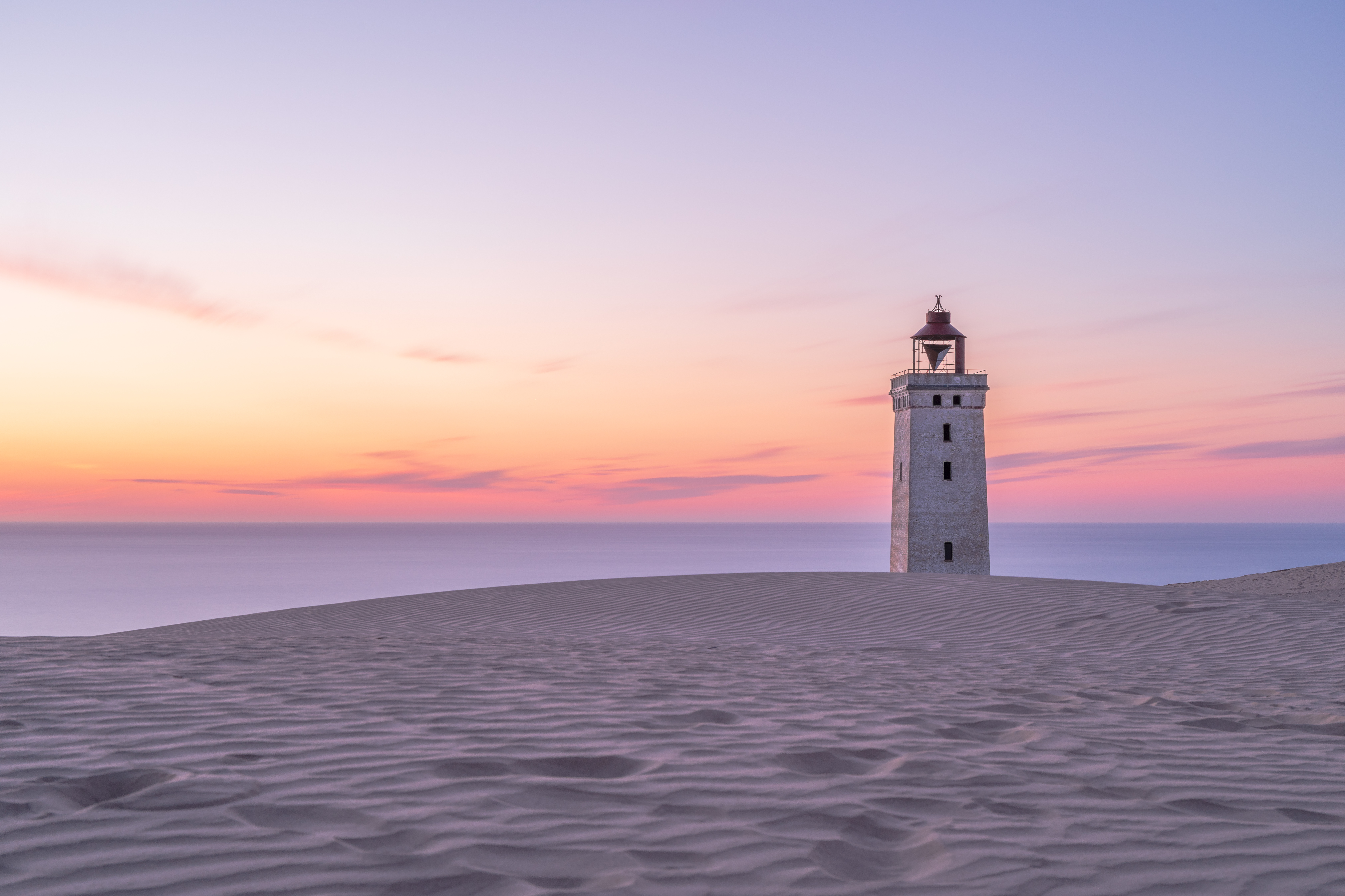 Rubjerg Knude Fyr is a lighthouse between Lønstrup and Løkken (municipality Hjørring) in Denmark which was built in 1900. From the 1910s, the wind blew large amounts of sand from the cliffs and the actual dune formed between the lighthouse and the sea. The dune moved towards northeast and now has completely passed the lighthouse. Of the outbuildings only loose bricks remains. The lighthouse was built 200 m from the coast, but the sea has since eaten into the 60 m high cliff so much that the lighthouse is now in grave danger of falling into the sea . It's now planned to move it 60-80 meters inland, which should protect it another 40-60 years.