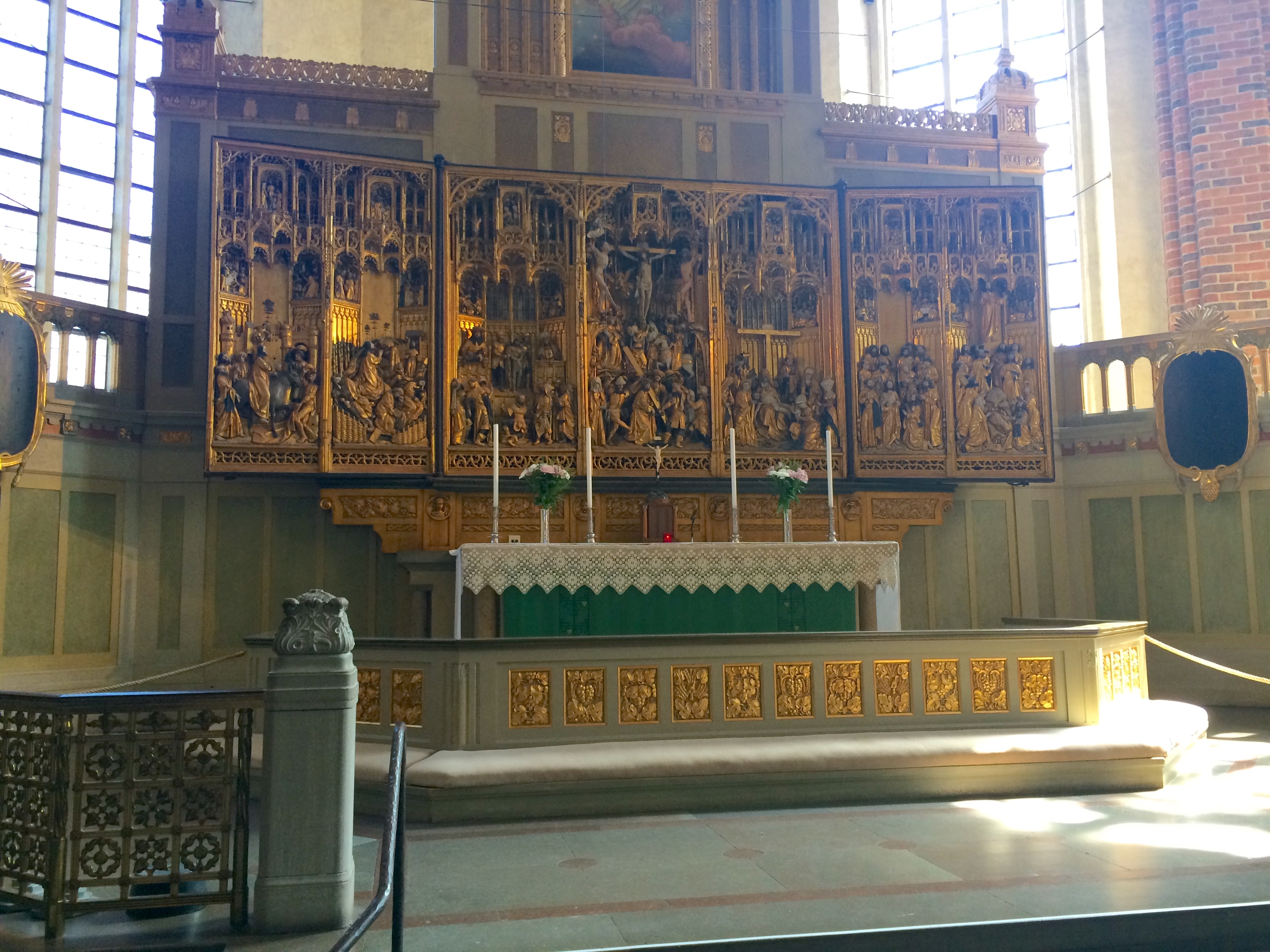 The high altar of Strängnäs Cathedral, Sweden, showing detail of the sanctuary, and the very large carved and gilded triptych reredos. The altar cabinet at the high altar from 1480-1490, with pictures from the gospel of Christmas and, when you opened the cabinet, the history of passion, made in Flanders and completed in 1490 in Brussels (in a workshop in Brussels). The cabinet is donated by Bishop Kort Rogge and is one of Sweden's largest altar cabinets. The ridge cabinet at the high altar of the cathedral is the largest and strangest of the church's medieval altar cabinets