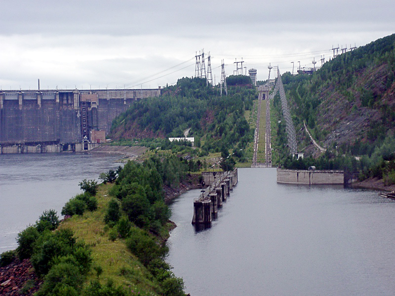 Boat lift on the Yenisei at Krasnoyarsk Dam in Russia. It serves to provide river vessels access to the Krasnoyarsk reservoir. The lift is designed as an electric rack railway with hydrostatic drive and punch rack. The route contains not only bridges, but also a gigantic turntable. The cog railway is about 2 kilometers long, transports ships up to 1500 t, overcomes a difference in altitude of 118 m and was completed in 1982. The power is supplied by four pantographs, which are mounted on two platforms and sweep the catenary that can be seen in the picture to the right of the route.