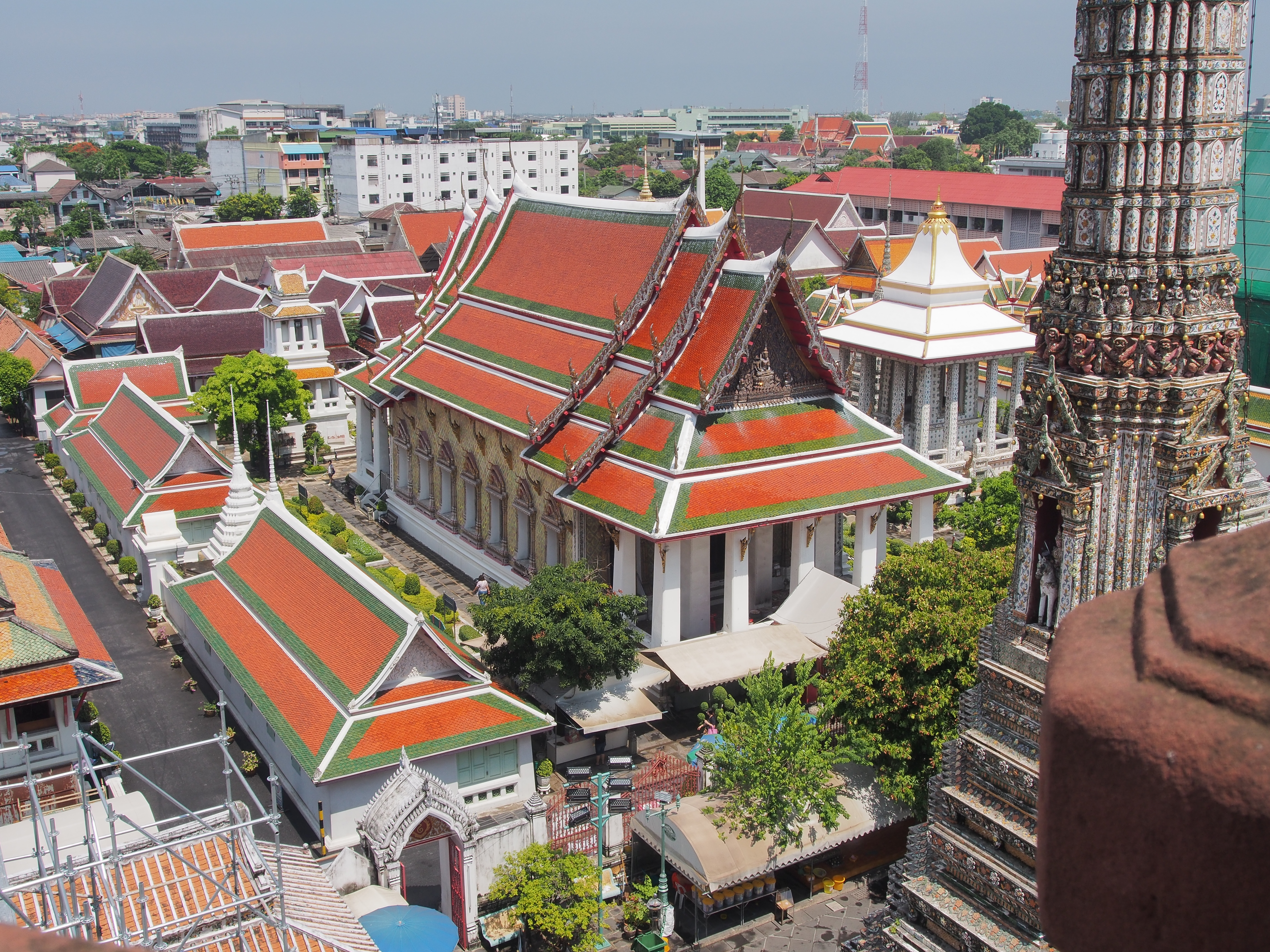 Wat Arun, the most iconic temple of Bangkok is located on Thonburi side of Bangkok, almost opposite to the Grand Palace and Wat Pho. Built during seventeenth century on the bank of the Chao Phraya river, its full name 'Wat Arun Ratchawararam Ratchawaramahawihan' is rather hard to remember so it is often called 'Temple of Dawn. The distinctive shape of Wat Arun consists of a central 'Prang' (a khmer style tower) surrounded by four smaller towers all incrusted with faience from plates and potteries. The stairs to reach a balcony on the main tower are quite steep, usually easier to climb up than to walk down, but the view from up there is really worth it.