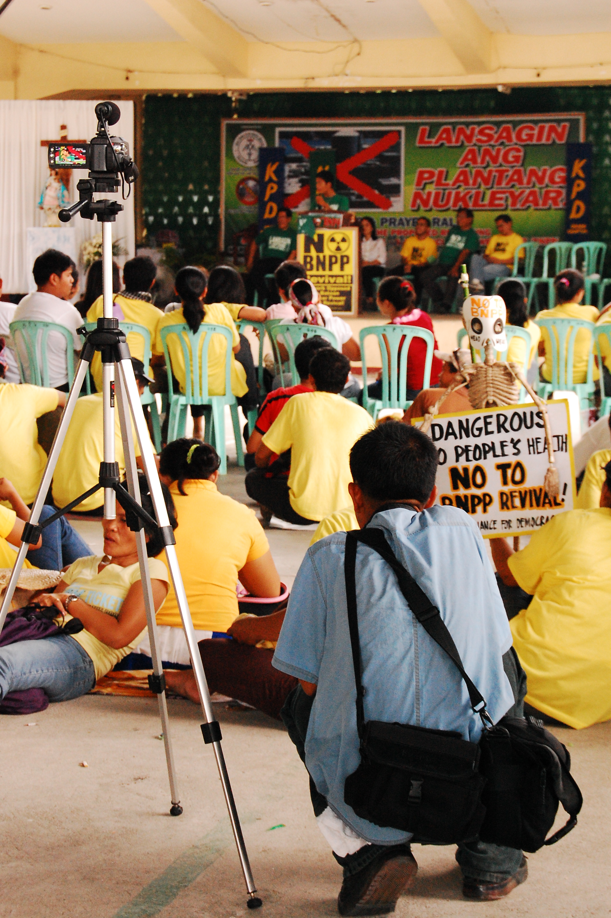 A speaker discusses the cons of the w:Bataan Nuclear Power Plant revival while being recorded on video. Amongst him are also against the plant's reopening. A skeleton toy can be seen in the photo, hinting terror and deadly danger. 
This was taken in a basketball court around Morong Parish Church Compound where a Catholic mass had been held hours before.
