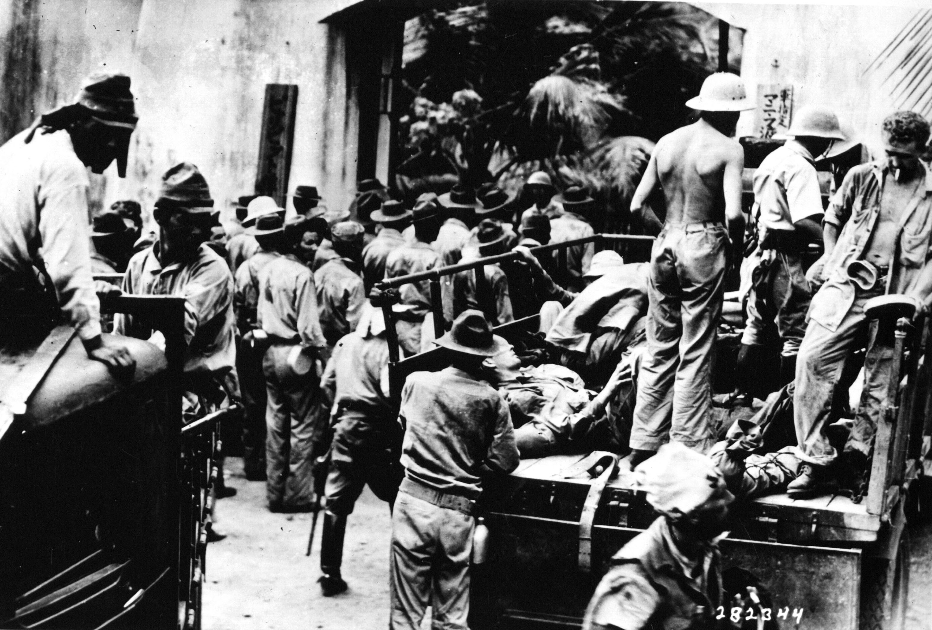 Scope and content:  Original Caption: American and Filipino prisoners, captured at Corregidor, arrive at Bilibid prison by foot and truck as Japanese look on. They were taken by boat to Cavite. Those unable to walk were hauled the distance of approximately 40 miles. The guards watch them help each other to the ground.