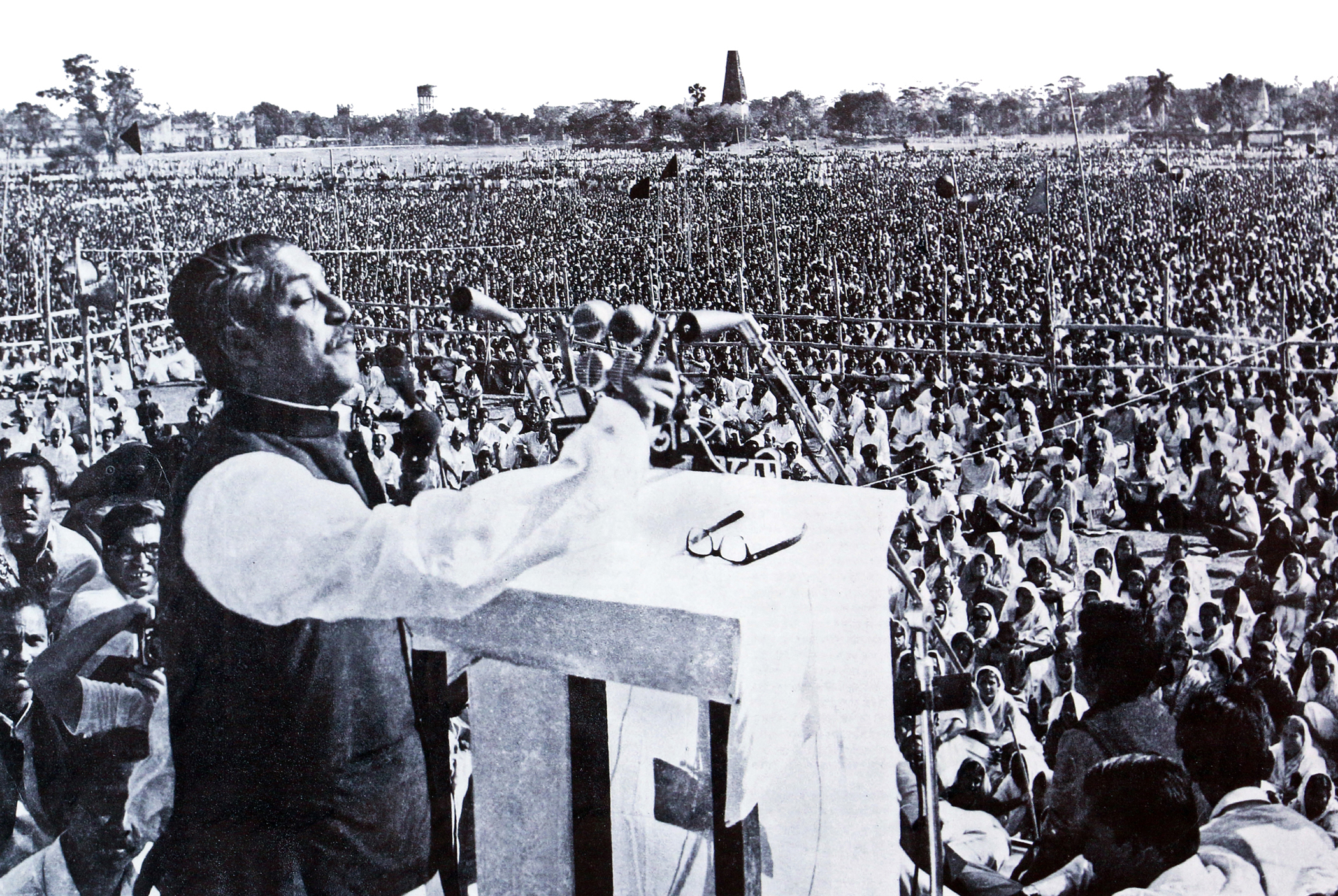 Photograph showing Sheikh Mujibur Rahman (also known as "Bangabandhu") delivering his historic speech "7 March Speech of Sheikh Mujibur Rahman" on 7 March 1971 at the then Ramna Race Course (now Suhrawardy Udyan), Dhaka, East Pakistan (now Bangladesh). The mass gathering can be seen behind him, as he raised his hand in address. This speech is widely regarded as the de-facto proclamation of Bangladesh’s struggle for independence.