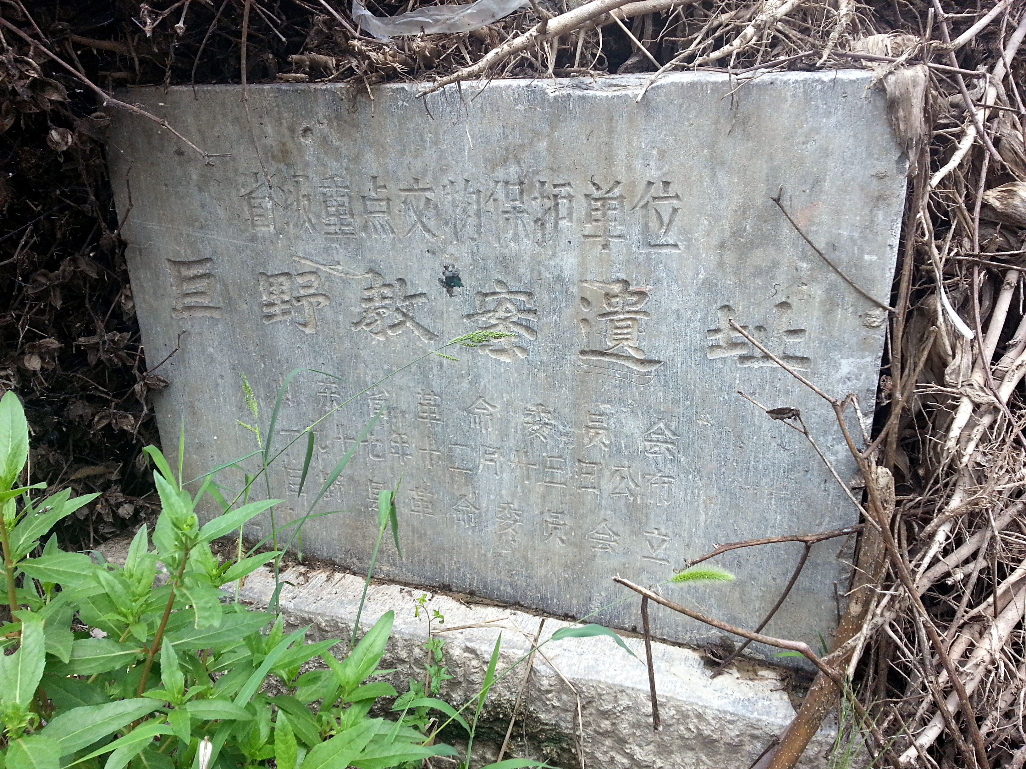 Photograph of the road-side marker near the site of the Juye Incident. The text of the inscription reads: 省级重点文物保护单位, 巨野教案遗址, 山东省革命委员会, 一九七七年十二月十五日公布, 巨野县革命委员会立. English translation: Provincial Key Cultural Relic Protection Unit, Site of the Juye Incident,Shandong Provincial Revolutionary Committee, Announced on December 15, 1977, Erected by the Juye County Revolutionary Committee