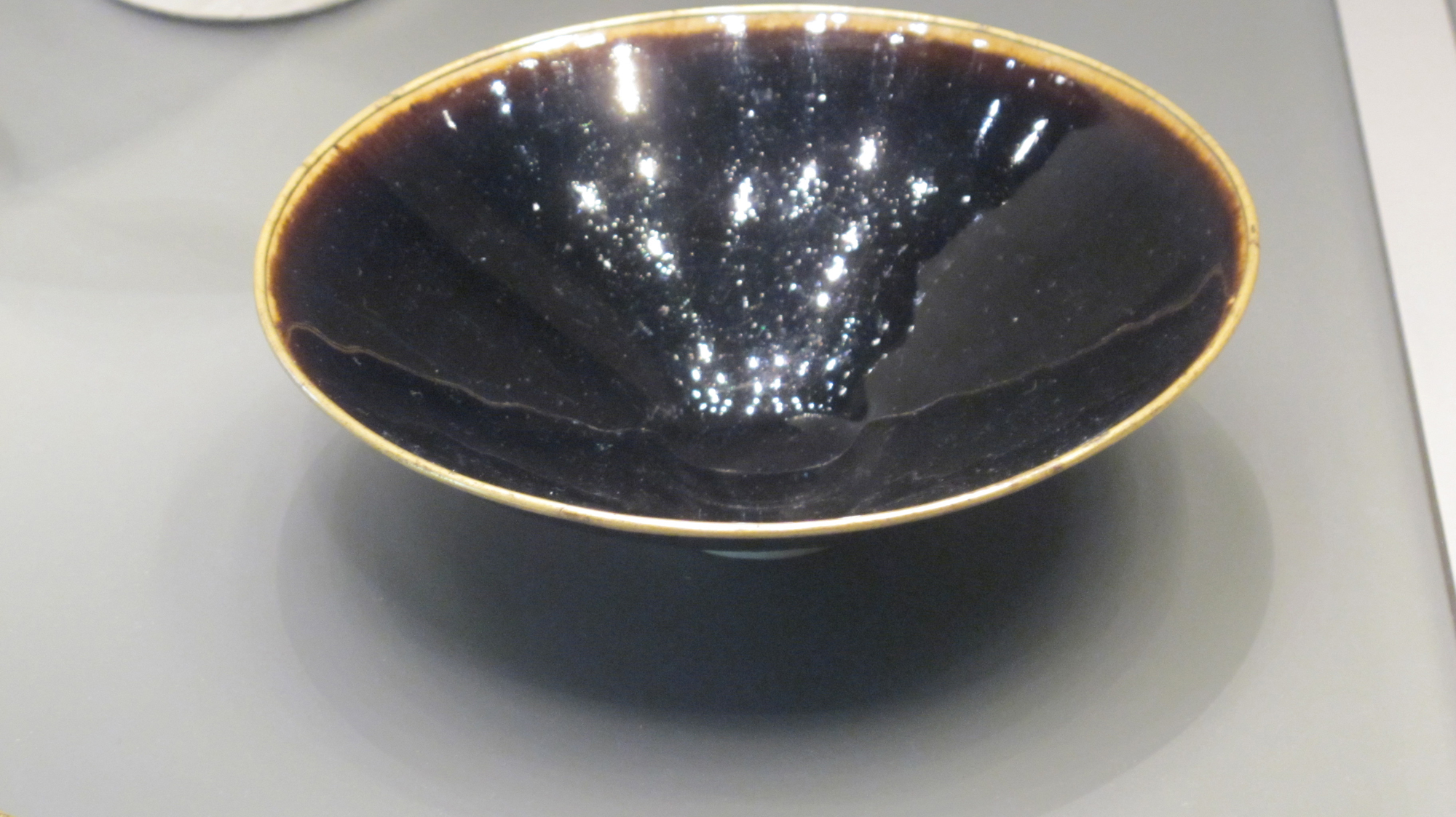 Black glazed tea-bowl. AD 1000-1127. Northern Song dynasty. Quyang, Ding prefecture, Hebei province.  Sir Percival David Collection, British Museum. Quotation of the museum : Ding potters manufactured vessels of exquisite quality with pure white bodies, but also added coloured glazes. This example is coated in a solution rich in iron-oxide which, when fired, gives it a glossy ink-black color. Song dynasty writers celebrated black and brown wares, associating them with luxurious lacquer wares. It has a copper rim which enhances its status.