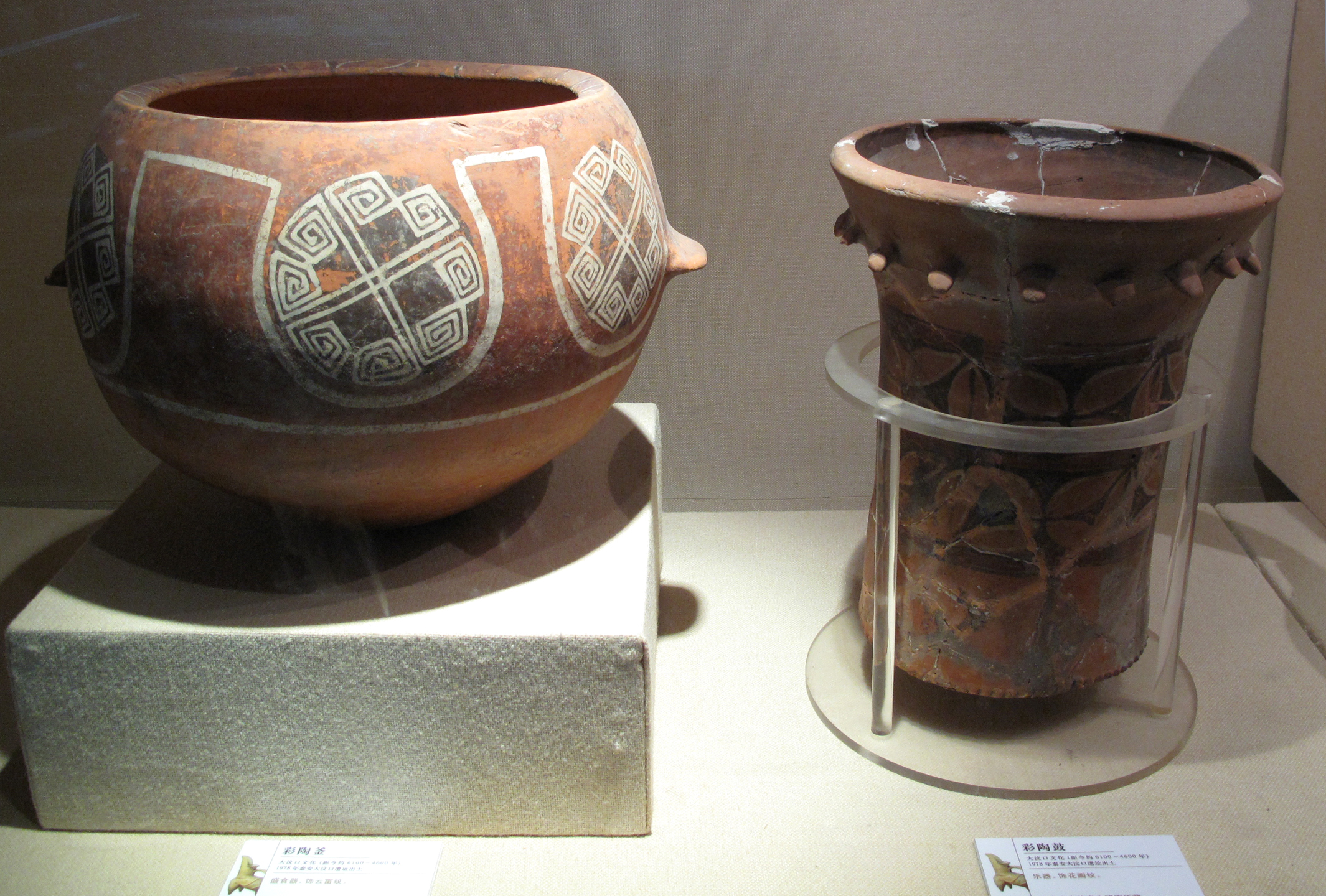 Neolthic Pottery. Dawenkou Culture, 4th millennium BC.
Shandong Provincial Museum, Jinan

A deep bowl and a drum are shown here. The main pattern on the bowl is formed by eight squared spirals that are connected by crossing diagonal arms. The drum is missing its drumhead, which could have been stretched taut over the top and attached at the lugs.