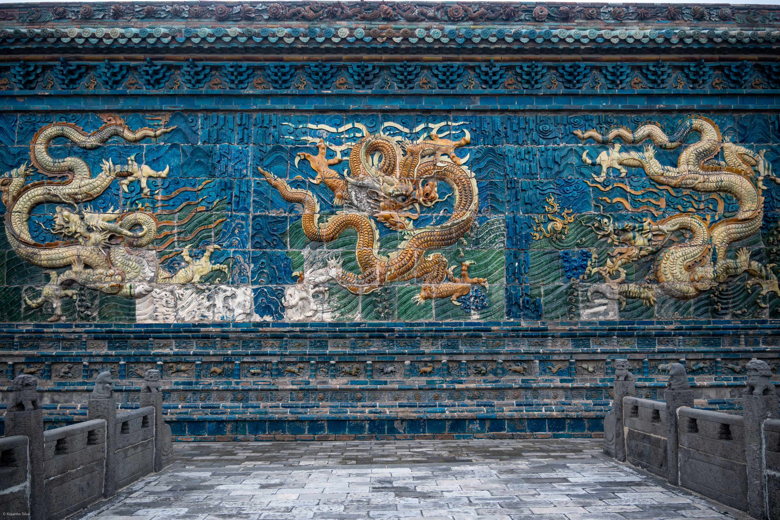 The Nine Dragon Screen in Datong, Shanxi, China, is a magnificent glazed-tile wall built in 1392 during the Ming Dynasty for Zhu Gui, the thirteenth son of Emperor Zhu Yuanzhang. It is the oldest and largest of China's three famous Nine Dragon Screens, adorned with 426 colorful ceramic tiles depicting nine vivid dragons amidst clouds, waves, and mountains. Originally placed in front of Zhu Gui’s palace to ward off evil spirits, it features a central golden dragon flanked by pairs of dynamic dragons, complemented by a pond that reflects their lifelike forms.