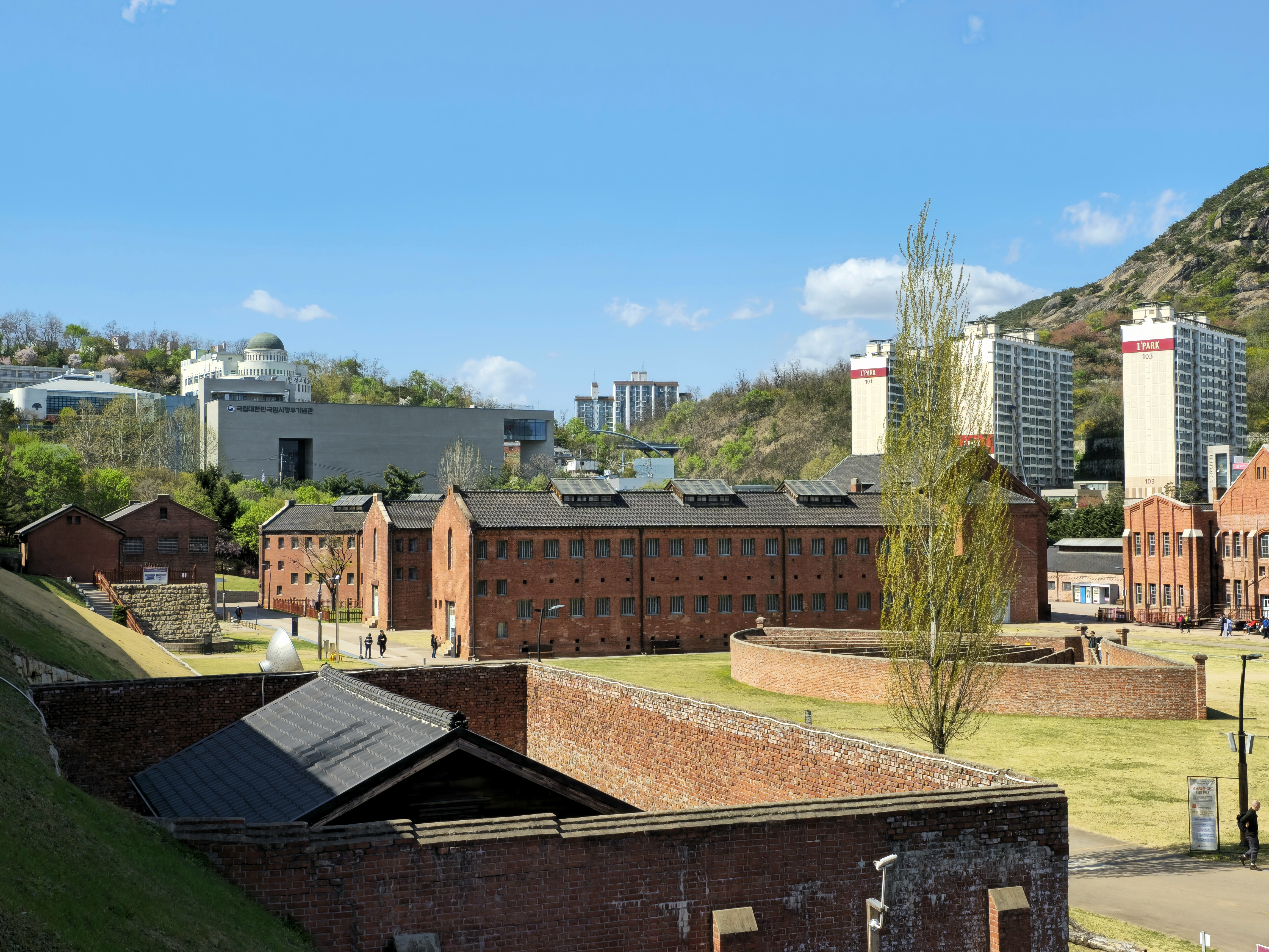 a Picture taken from Seodaemun Independence Park. In this picture, starting from the bottom left and going counterclockwise, Seodaemun Prison Hall, National Memorial of the Korean Provisional Government, Hansung Science High School, Muakjae, Mountain Inwang and Inwangsan IPark Apartment complex are shown.