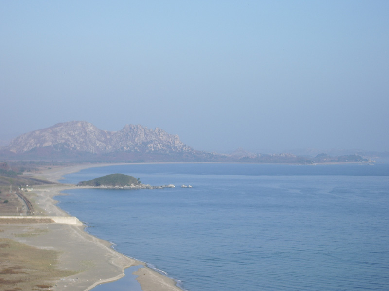 The turtle-shaped rock in the center left is the end of South Korean jurisdiction.
The peaks in the distance, and the peninsula jutting to the right, are North Korea.
The area in between is the Demilitarized Zone.
On the peninsula there is a small village visible. I was told that it was an empty propaganda village, just like dozens of others North Korea maintains along the border.

The beach looks lovely, and very inviting for a stroll. But it is safe to assume that landmines are everywhere down there, so even after permanent peace comes to the Korean peninsula, I can forget about a stroll down there.