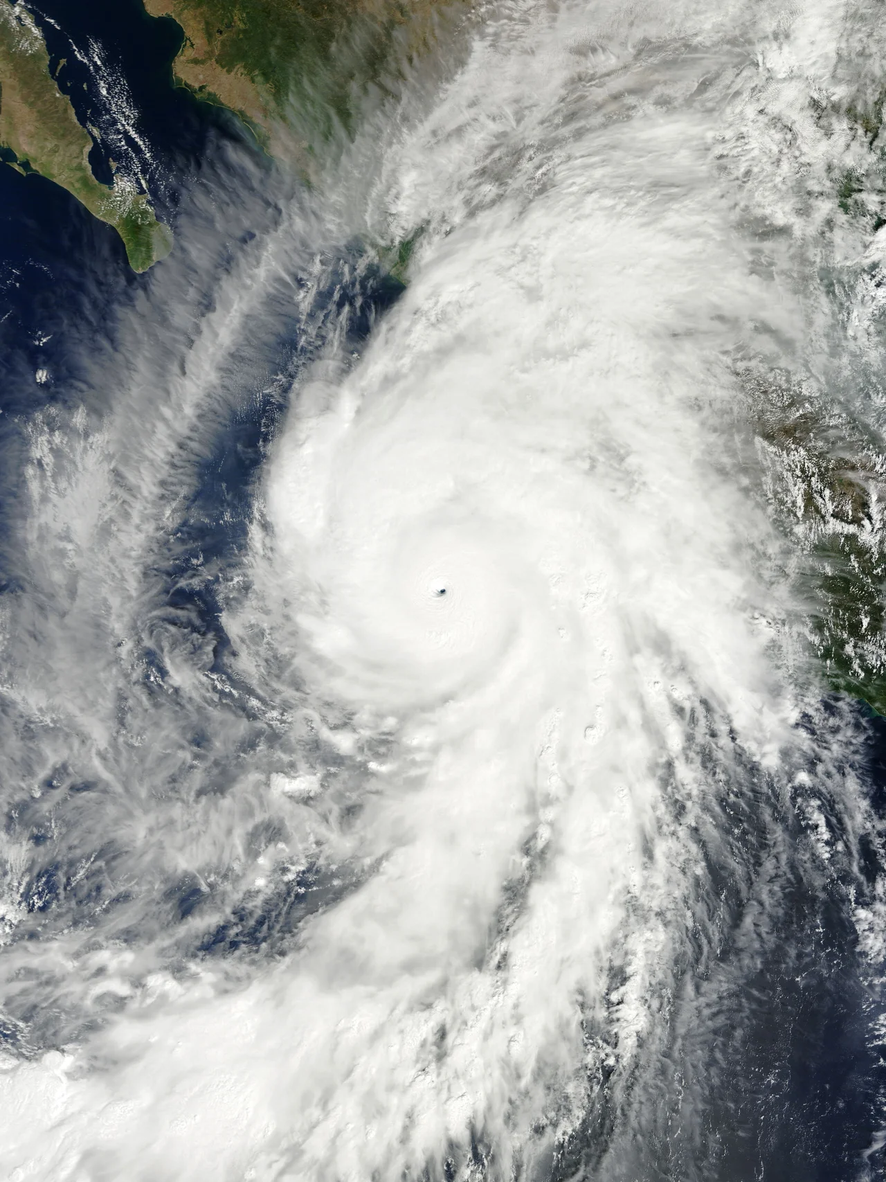 Before the year 2004, only two tropical cyclones had ever been noted in the South Atlantic Basin, and no hurricane. However, a circulation center well off the coast of southern Brazil developed tropical cyclone characteristics and continued to intensify as it moved westward. The system developed an eye and apparently reached hurricane strength on Friday, March 26, before eventually making landfall late on Saturday, March 27, 2004.
The crew of the International Space Station was notified of the cyclone and acquired excellent photographs of the storm just as it made landfall on the southern Brazilian state of Santa Catarina (the storm has been unofficially dubbed “Cyclone Catarina”). Note the clockwise circulation of Southern Hemisphere cyclones, the well-defined banding features, and the eyewall of at least a Category 1 system. The coastline is visible under the clouds in the upper left corner of the image.