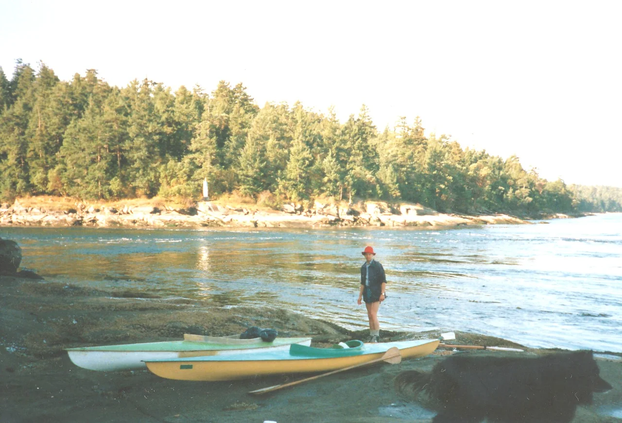 Tidal currents through Dodd Narrows can be 7-8 knots. False Narrows, to the east of Mudge Island, has lesser currents and is usually the choice of kayakers going to the southern Gulf Islands from Nanaimo.
The kayaker pictured here is visiting from Austria. The kayaks are both the venerable Frontiersman brand made in the '60's in BC. The white one, on being repaired from damage, had the cockpit modified to the extent of allowing room for the dog seen in in the foreground shadow. She logged many miles in it.