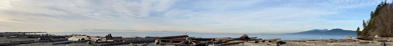 Wreck Beach on a sunny winter day, showing the wood logs and Vancouver island as well as Bowen Island over the sea.
