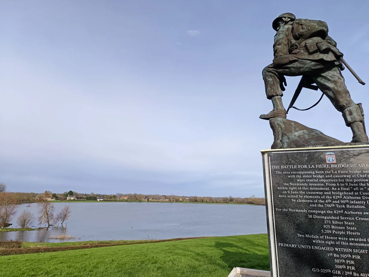 Iron Mike, statue de bronze d'un parachutiste regardant vers les marais de Merderet. Elle a été dévoilée le 7 juin 1997 et une statue jumelle est visible à Fort Benning. La plaque sur le socle décrit la bataille de la Fière entre le 6 et le 9 juin 1944, avec les unités engagées, le nombre de victimes et les médailles militaires décernées.