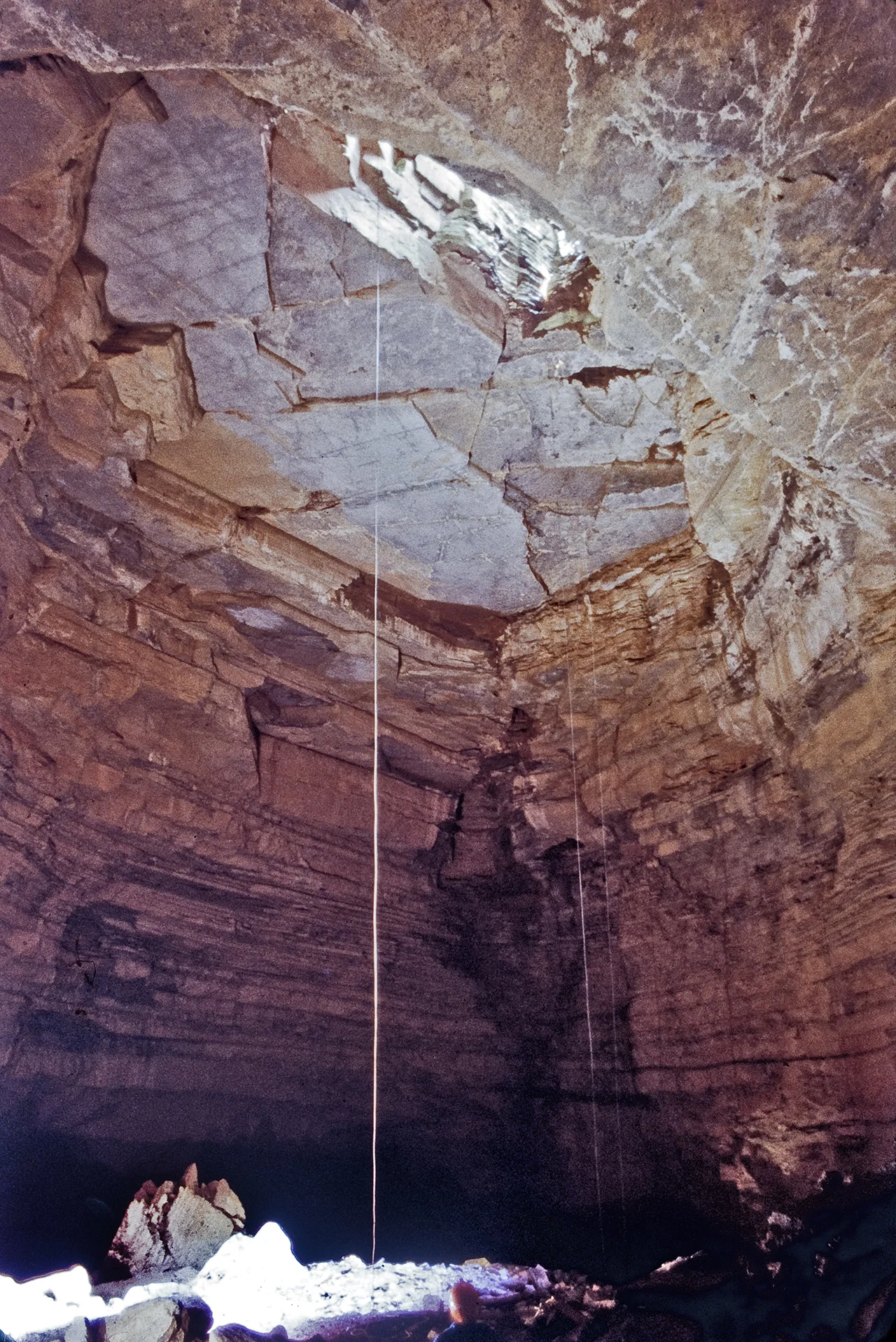 Pit entrance to Hellhole cave in West Virginia. Caver in orange helmet visible at the bottom of the ropes.