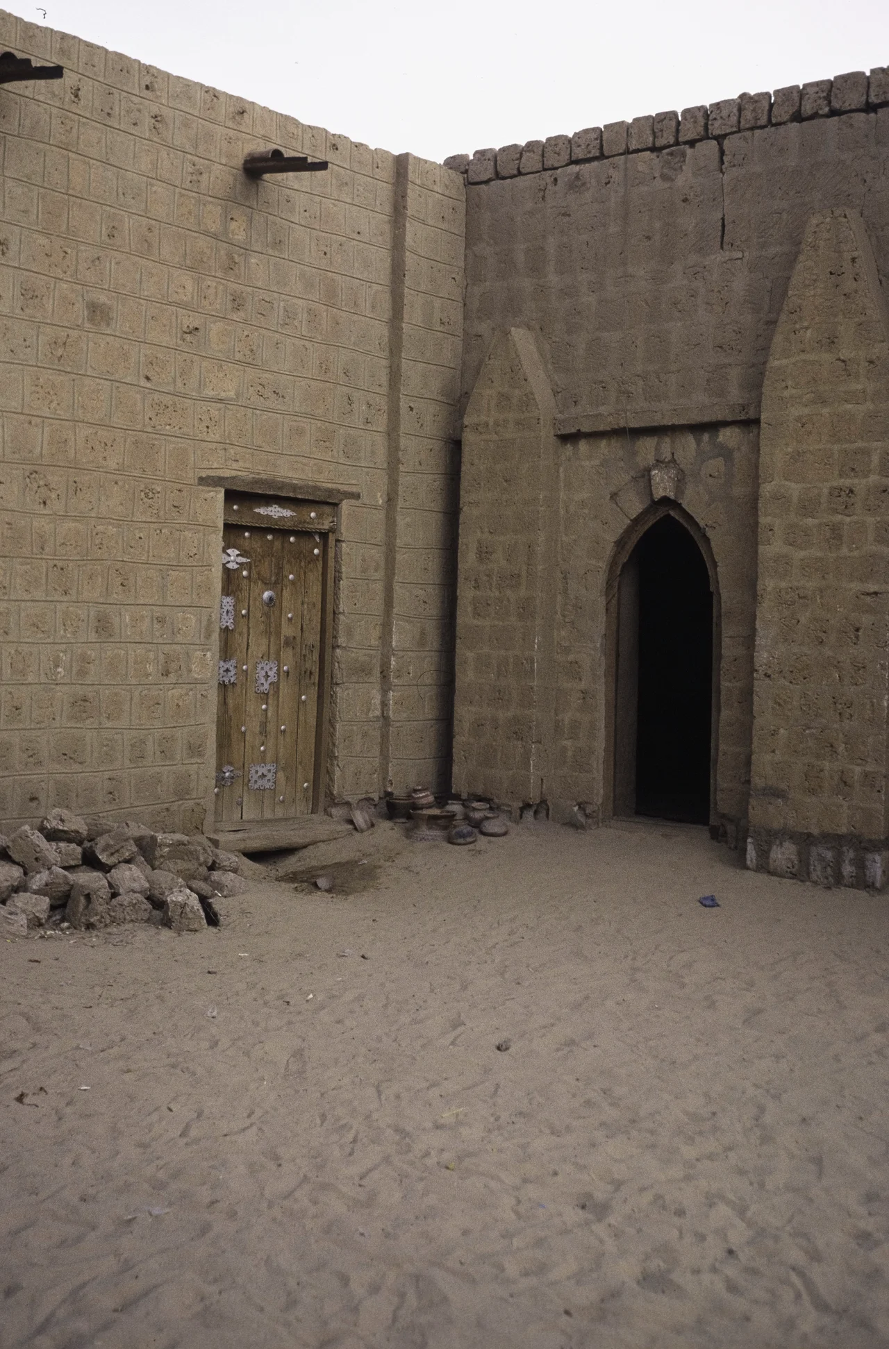 An entrance to the Sankoré Mosque. A corner of a square with a wooden door and a pointed gate. The Djinguereber, Sankoré and Sidi Yahya mosques together constitute the University of Timbuktu.