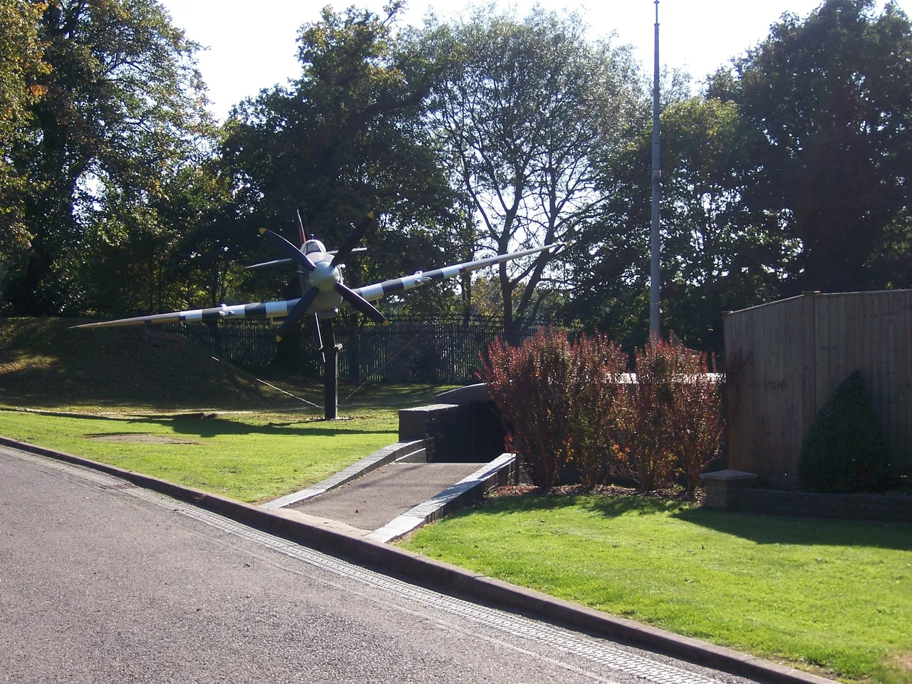 Entrance to the Battle of Britain Bunker with Spitfire gate guardian.
This a glass fibre replica Supermarine Spitfire IXc FSM (Merlin 61 engine), currently in the colours of s/n BS239 5R-E.[1]. It originally represented BR600 SH-V flown by Flight Lieutenant Donald Kingaby, No. 64 Squadron RAF. This was the first recorded Mark IX to shoot down an enemy aircraft, a Focke-Wulf FW-190, in July 1942.[2]