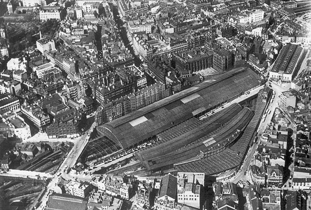 Aerial view of the Victorian station at New Street, Birmingham, UK. The original LNWR station (opened in 1854) with its large arched roof is at the north, while the curved Midland Railway extension (opened 1885) is to the south, the access road in between them is Queen's Drive.