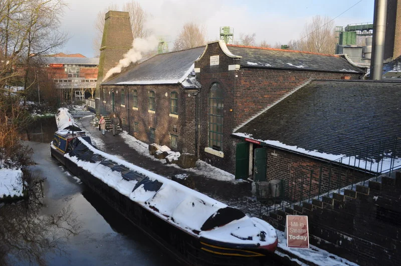Etruria Industrial Museum, near to Hanley, Stoke-on-Trent, Great Britain.
Jesse Shirley's Bone and Flint Mill between the Caldon and Trent & Mersey Canals, Stoke on Trent (this small arm is on the T&M). The low part of the building houses the boiler, to the left of it is the beam engine house. This then leads onto the mill, top floor is the pan room and bottom the gears. The 'chimney' on the end is a flint calciner/kiln.
To the upper right of the picture the Jesse Shirley's company is in modern premises still producing calcined bone ash to the potters.