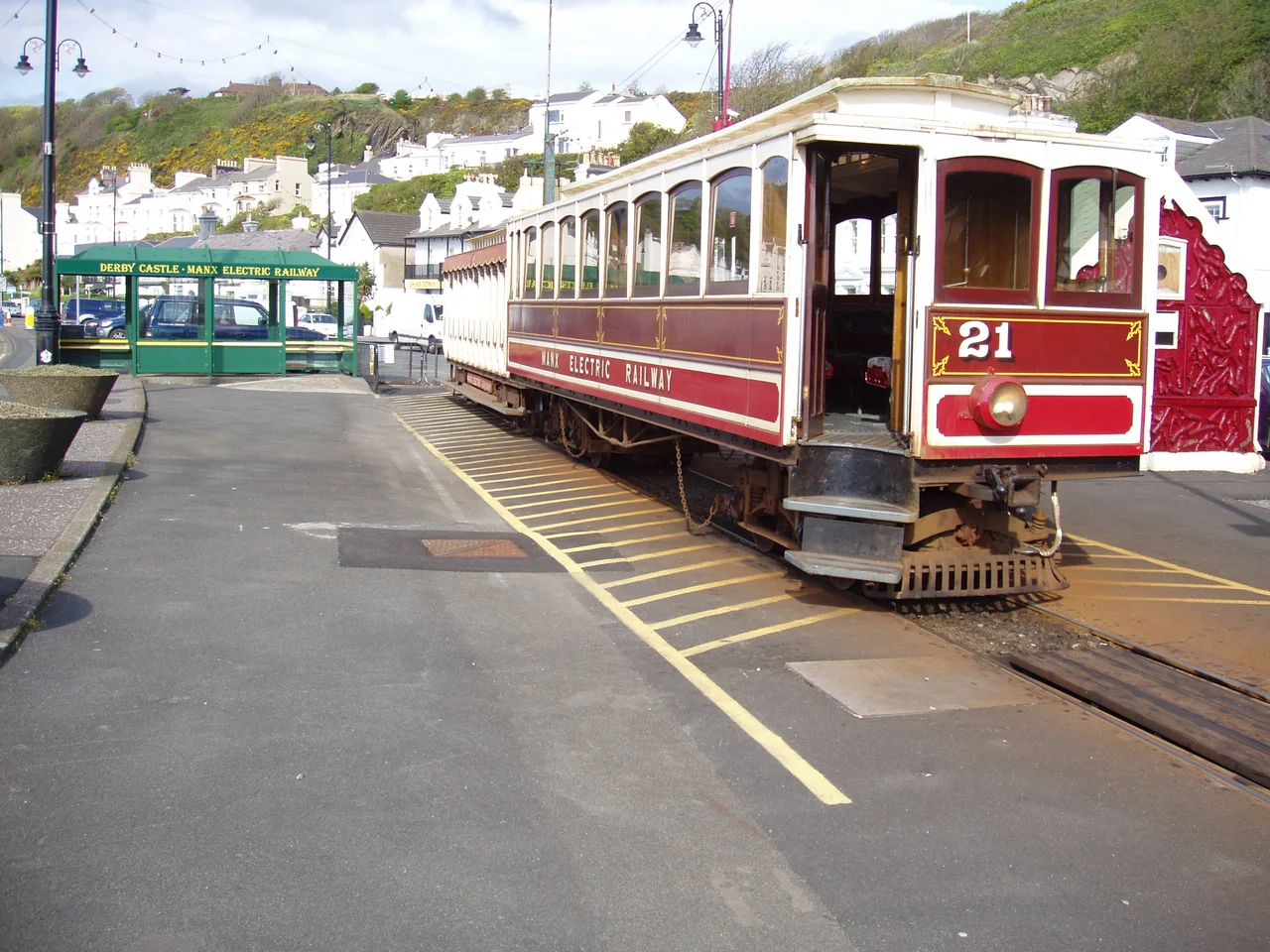 Winter saloon car 21 stands by at the Derby Castle tram station, the southern terminus the Manx Electric Railway. The waiting shelter (green) and parking lot are on the left while the ticket sales kiosk (red) can be seen on the right. This is on the far east end of Douglas, Isle of Man.