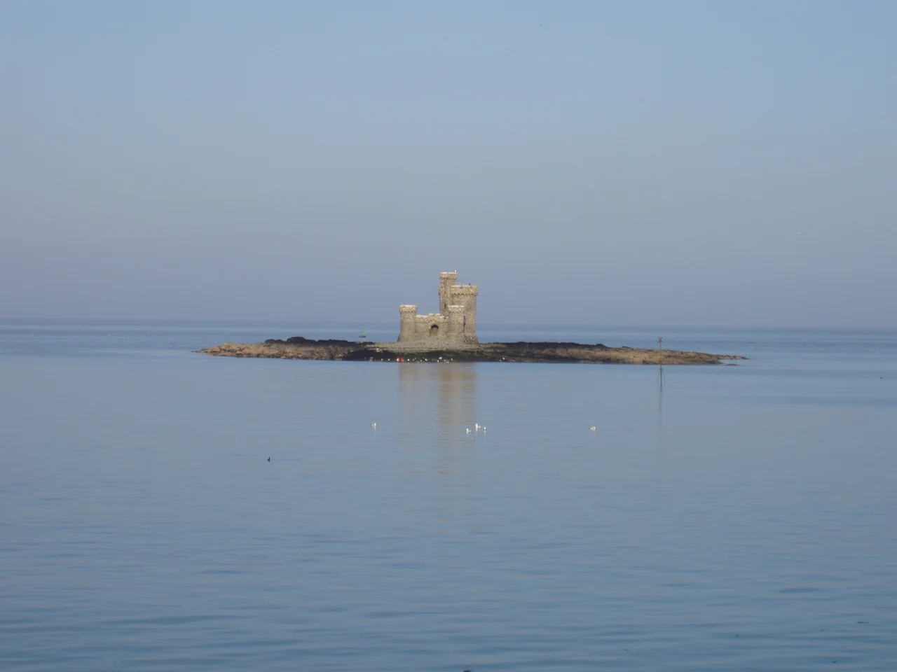 The Tower of Refuge stands upon St. Mary's Isle (also known as Connister Rock) - a marine hazard upon which many ships approaching Douglas Harbour wrecked due to low visibility or bad weather. The miniature castle was built in response to the 1830 destruction of the packet St. George with local donations. The project, undertaken by Sir William Hillary and designed by architect John Welch, was completed in 1832 and increased the visibility of the waterway hazard as well as provided a storage place for dry provisions in case anyone shipwrecked upon the isle. The islet is seen here at an average tide. Low tide allows one to walk out from the Douglas shore. Extremely high tide will completely submerge the islet from sight except for the Tower of Refuge.