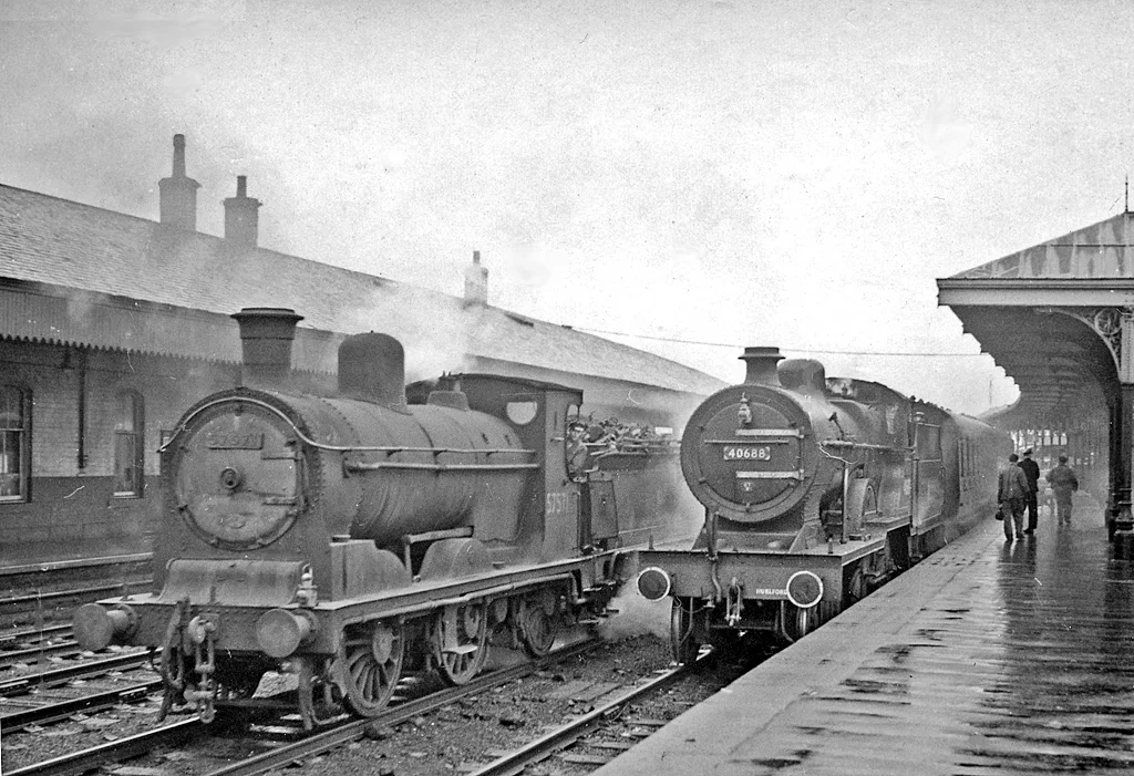 Local passenger and goods trains at Kilmarnock Station in 1957.
View east, towards Dumfries and Carlisle by the main line, also Muirkirk; ex-Glasgow & South Western. The local is the 17.15 to Glasgow St Enoch, with LMS 2P 4-4-0 No. 40688; the Up empties has ex-Caledonian 3F 0-6-0 No. 57571 built in 1899. Note the white-painted features on the 4-4-0, characteristic of locomotives repaired at St Rollox Works.(It was raining, as usual).