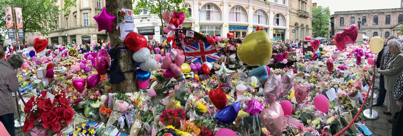 A panorama picture of the floral tribute to the victims of the 2017 Manchester Arena bombing at St Anne's Square in Manchester city centre. The picture was taken from the west side of St Anne's Square, with Exchange St visible to the left-hand side and St Anne's Church to the right-hand side.