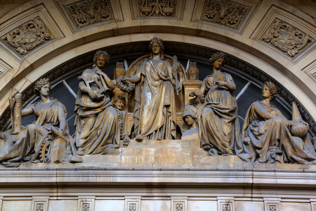 The centre figure represents Leeds and the four female figures below and on either side of her (looking from left to right) are Manufacture, with a loose roll of textile, a mallet, an anvil, a cog and pincers; Music and Poetry, with a lyre under one arm, and a trumpet or horn in the other; the Fine Arts with a palette in one hand; and Science, with a compass, a globe, what looks like a press of some kind, and a cone behind her. Two owls, emblematic of the city, sit on the twin pedestals near the middle, beside which are also a kneeling figure that looks like Pan, on the left, and a bust of Athena, on the right.
The side panels, show a little boy with a ram draped over his shoulders, signifying the importance of the wool trade to Leeds. The foliage is woven around other emblems of order, prosperity, etc.


 John Thomas (1813-62).