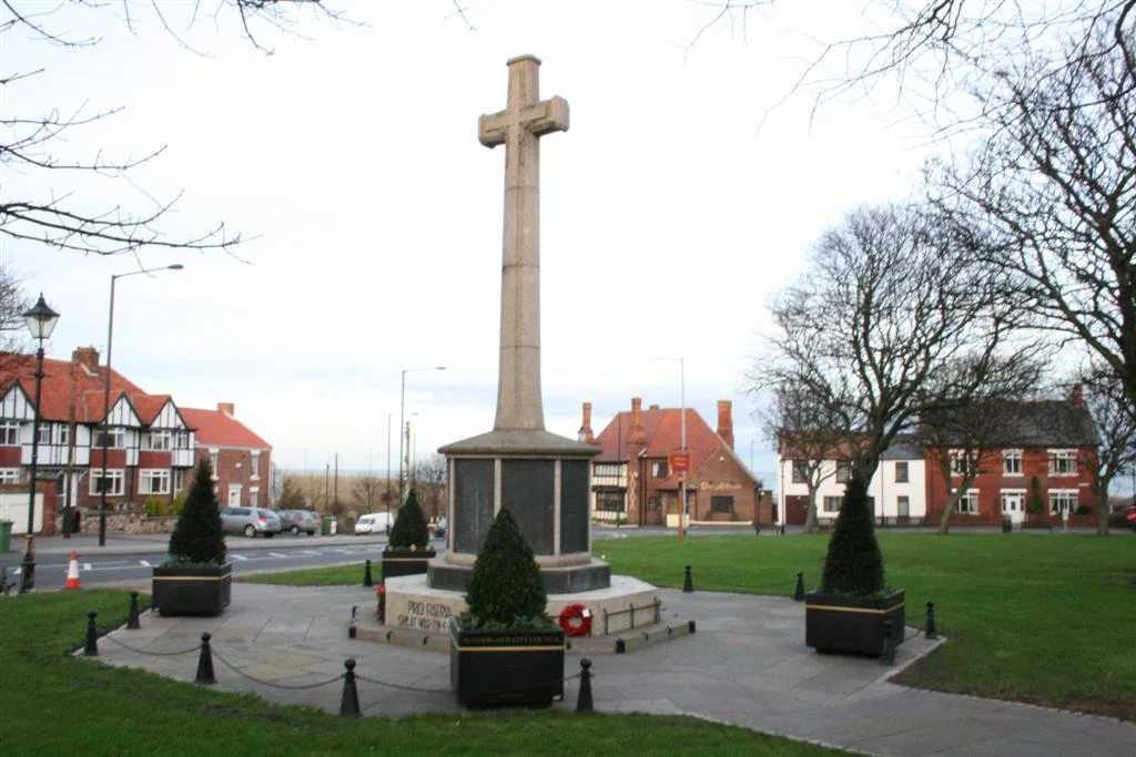 Photo of Ryhope village Green, facing East showing the World War I war memorial. In the background a wooden "Ryhope Village" sign can be seen.