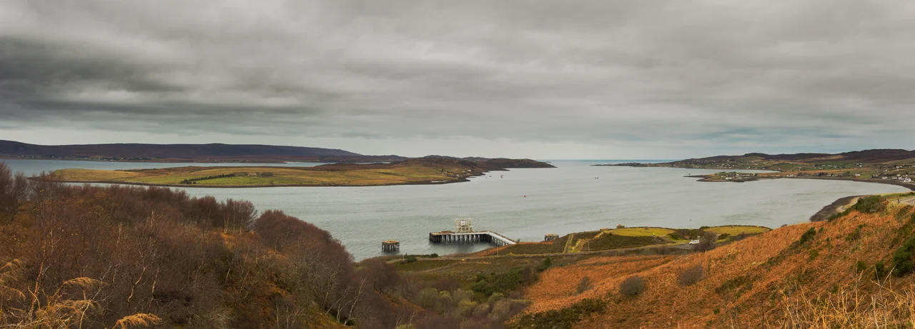 Panorama overlooking Loch Ewe. The NATO Petroleum, Oil and Lubricants (POL) depot can be seen in the foreground; the villages of Aultbea, Ormiscaig and Mellon Charles are visible along the Western shore of the loch (right hand side); North of the POL depot is the Isle of Ewe and in the background on the left hand side behind the island, part of the Eastern shore are visible, including the beach at Firemore.