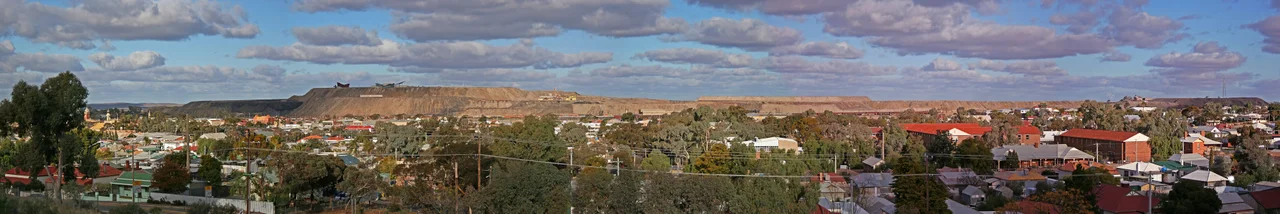 Panoramic view of the main section of the town of Broken Hill, NSW, Australia. Behind the town centre can be seen the man-made mullock heaps built from the waste rock from the Line of Lode mine that dissects the town (the mullock heaps are the "hills" that stretch almost the full width of this image). Over 800 workers lost their lives working the mines on the Line of Lode; a Miner's Memorial dedicated to their memory can be seen at the top of the left end of the mullock heap.
