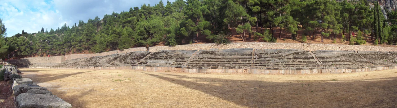 The starting line at the stadium used for the Pythian Games at Delphi, Greece. This starting line has a design representative of that of many ancient Greek stadiums: stones with two lines in which the athletes nudged their toes, and round holes in which posts could be erected to support the start signalling mechanism.
The stone steps for sitting the public behind were erected under the Romans.