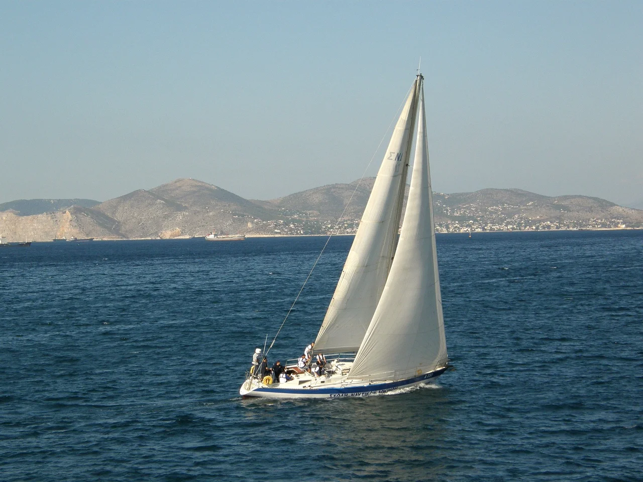 Sloop "MAISTROS" A233 of the Hellenic Naval Academy sails past Piraeus Peninsula, Greece, with a crew of naval cadet officers (midshipmen).