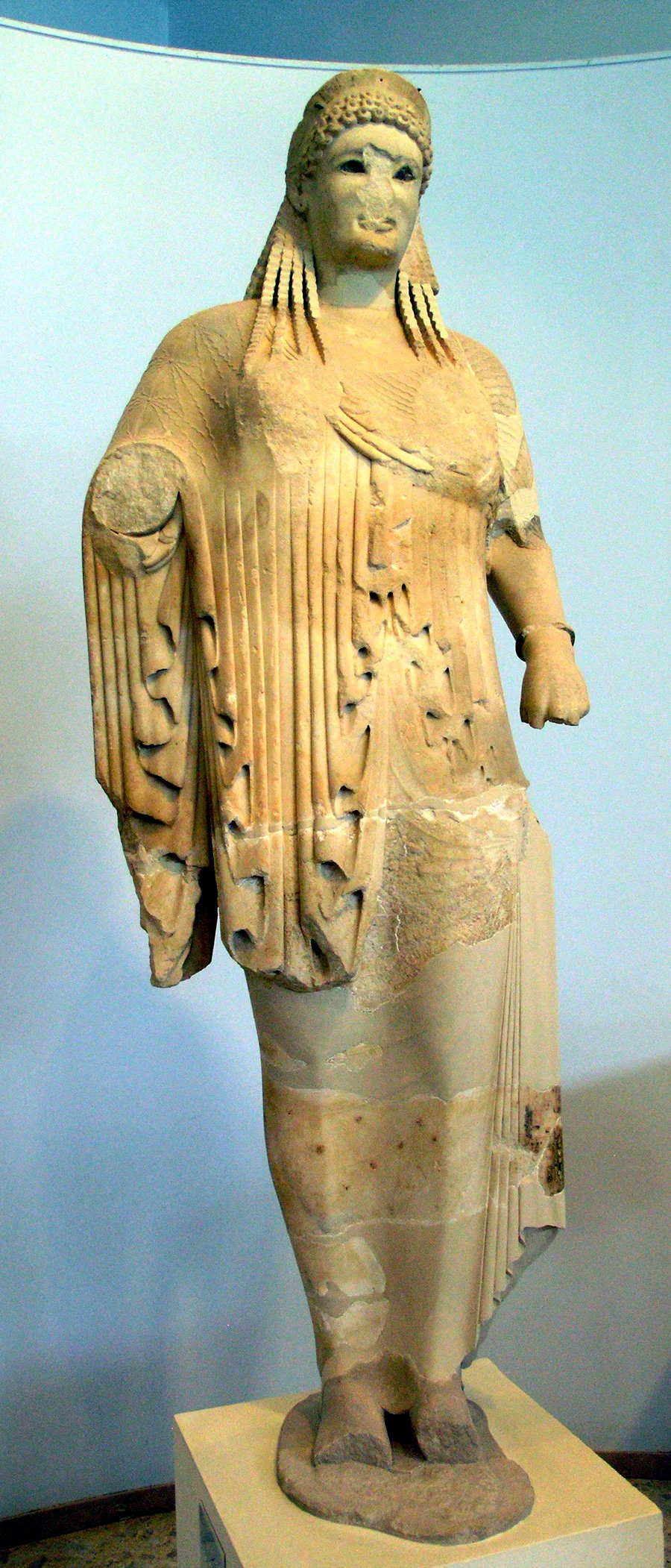 Statue of a larger than life-size korè, in Paros marble. She wears a chiton and himation, tiara with painted meanders, and bronze hair ornaments. Her eyes are set with rock crystal. The work has been dated around 520 B.C. (H.E.9580) and is associated with an epigraphic text. According to the inscription, the potter Néarchos dedicated the statue and the sculptor Anténor made it.