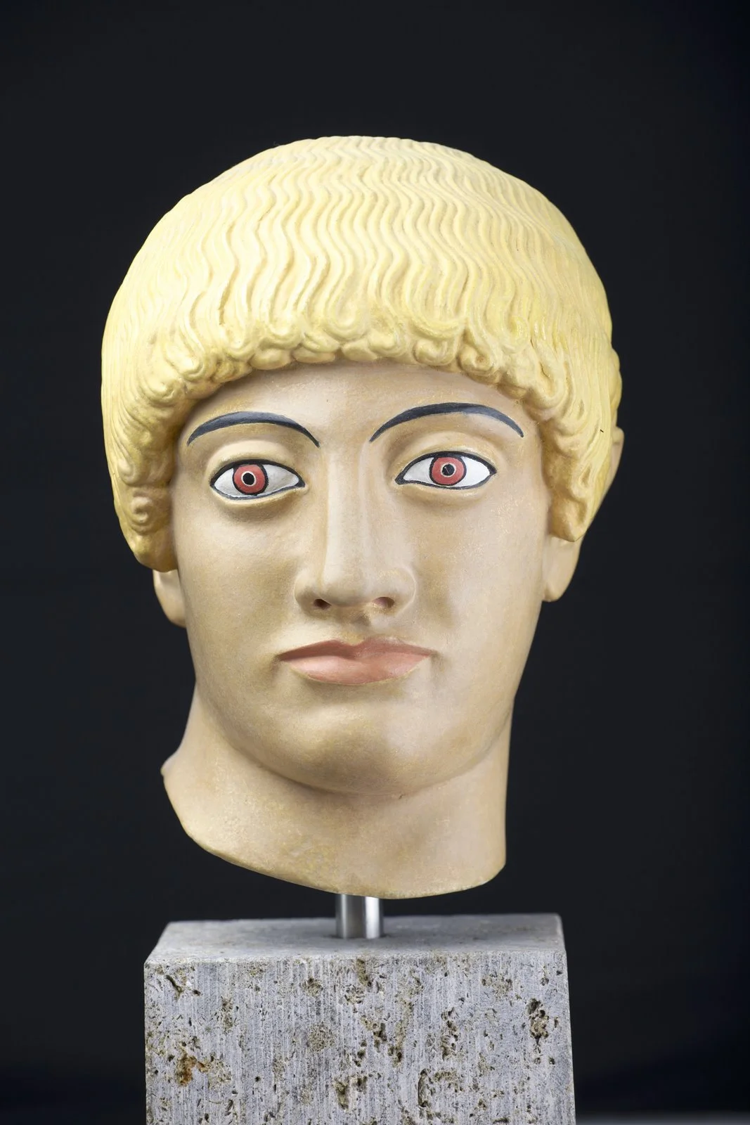 This is a photograph of the so called Blond Kouros's Head of the Acropolis. The head is a gypsum copy of the original in Athens. It is painted with the colors believed to have been originally used by the artist, however, only traces of the blond hair have been actually found. The painting was done by experts in the Antikensammlung München, Germany. Frontal view.