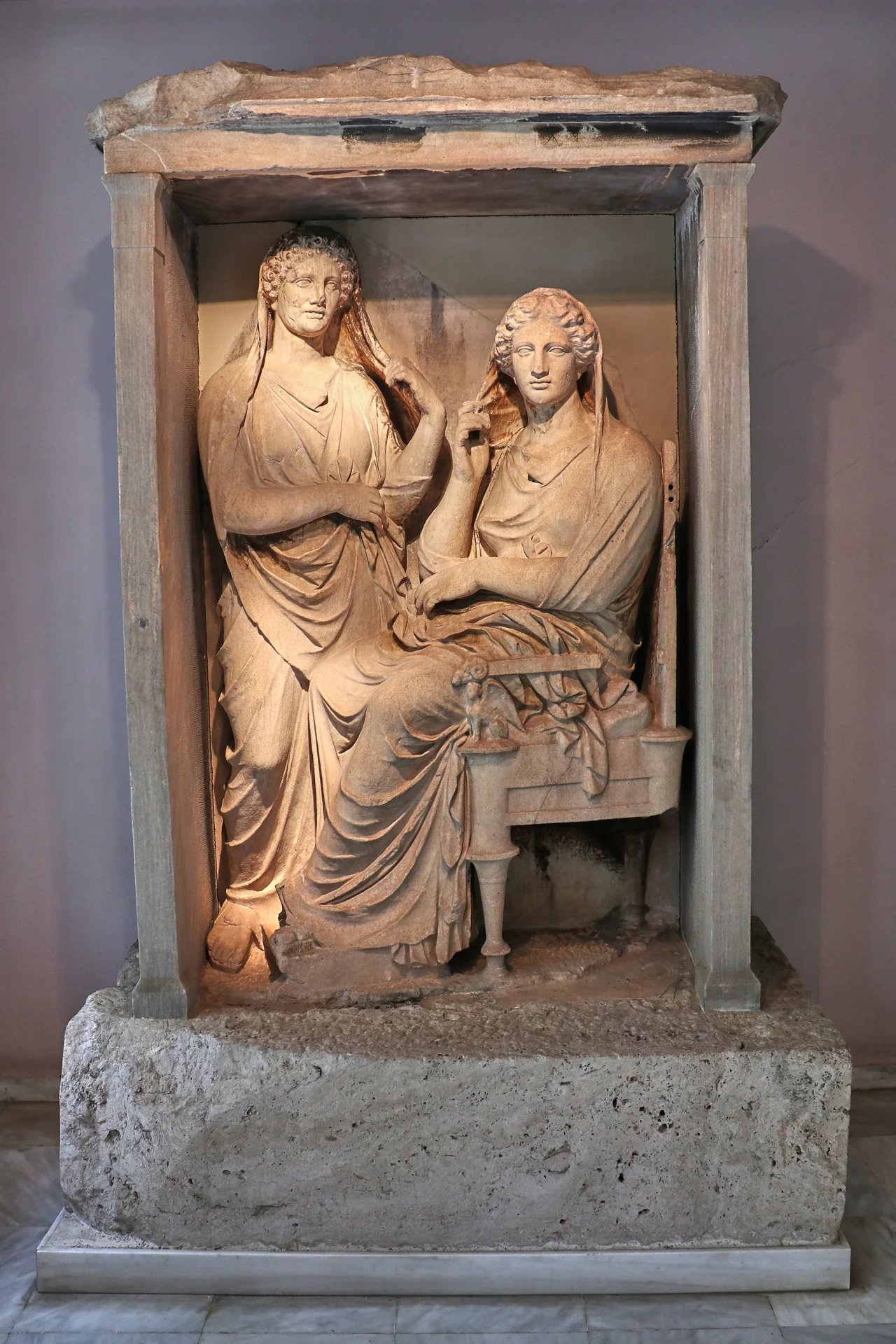 The inscription beneath the pediment gives the names of the two dead sisters. The women, remote and isolated, gaze apathetically at the spectator. They are already in another, transcendental world, far from the things of this life. The pilasters of the naiskos have been restored. It is one of the last tomb stones made before the law passed by Demetrius of Phaleron prohibiting the erection of luxurius tomb monuments. Ca. 325-310 B.C. From a grave enclosure by the South Way. Accession number: P 687. Archaeological Museum of Kerameikos. Athens, Greece. 
Text: Museum inscription.